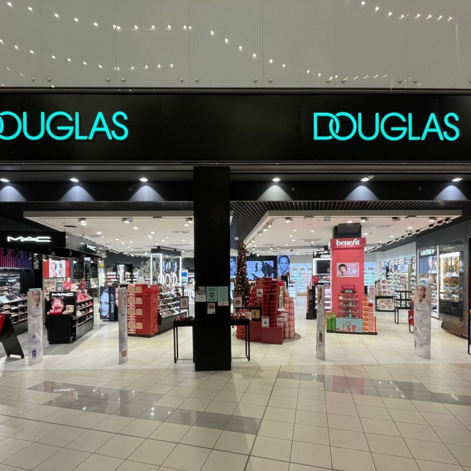 Pohľad na predajňu Douglas s výrazným logom v tyrkysovej farbe nad vchodom, lákajúci na nákupy kozmetiky a parfumov.