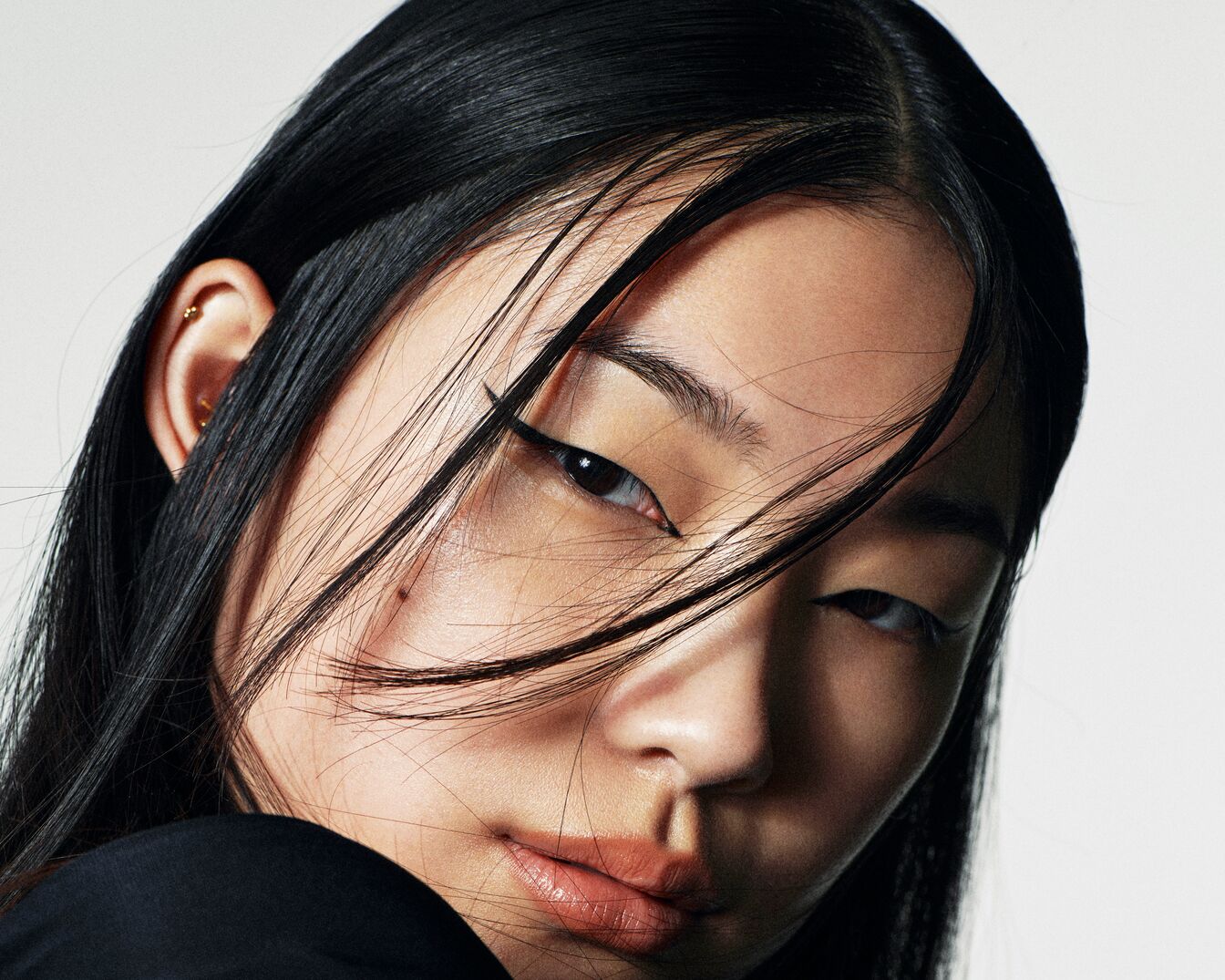 Közeli kép egy fekete hajú, fekete felsőt viselő nőről, aki finom tusvonallal emeli ki a szemét.