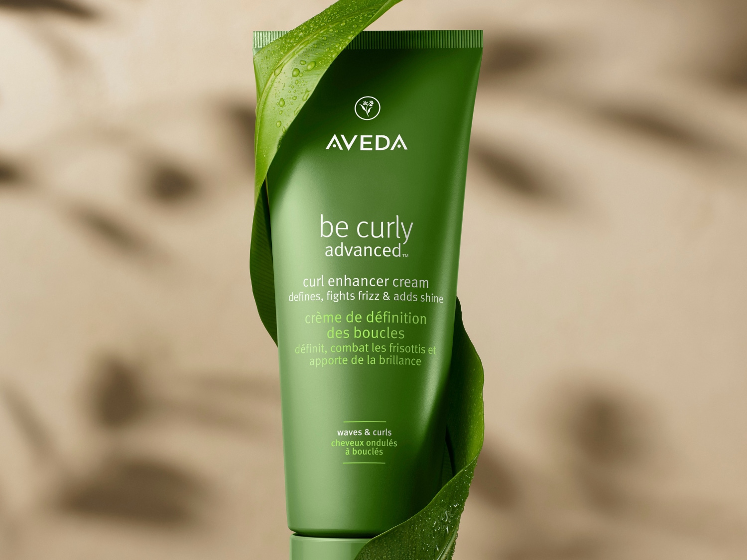 Groene tube Aveda Be Curly Advanced krulversterkende crème, die krullen definieert, pluis tegengaat en glans toevoegt, omwikkeld door een groen blad.