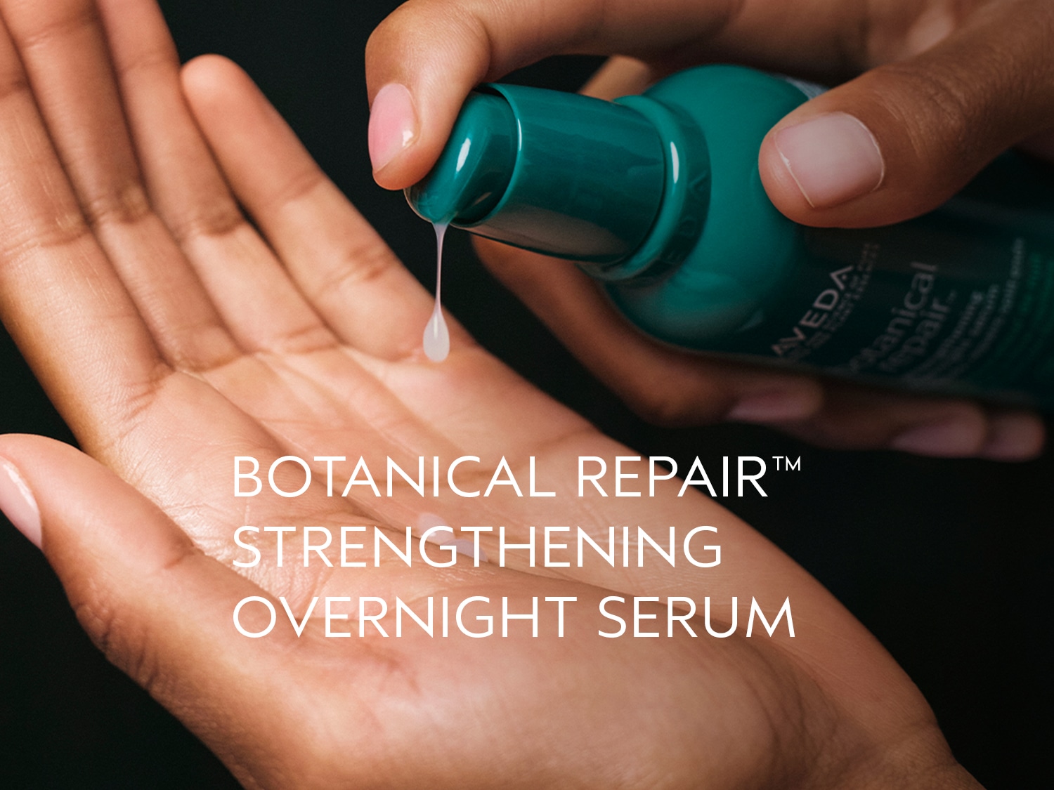 Een hand houdt een groene fles Aveda Botanical Repair Strengthening Overnight Serum vast, terwijl een druppel serum in de open handpalm valt.