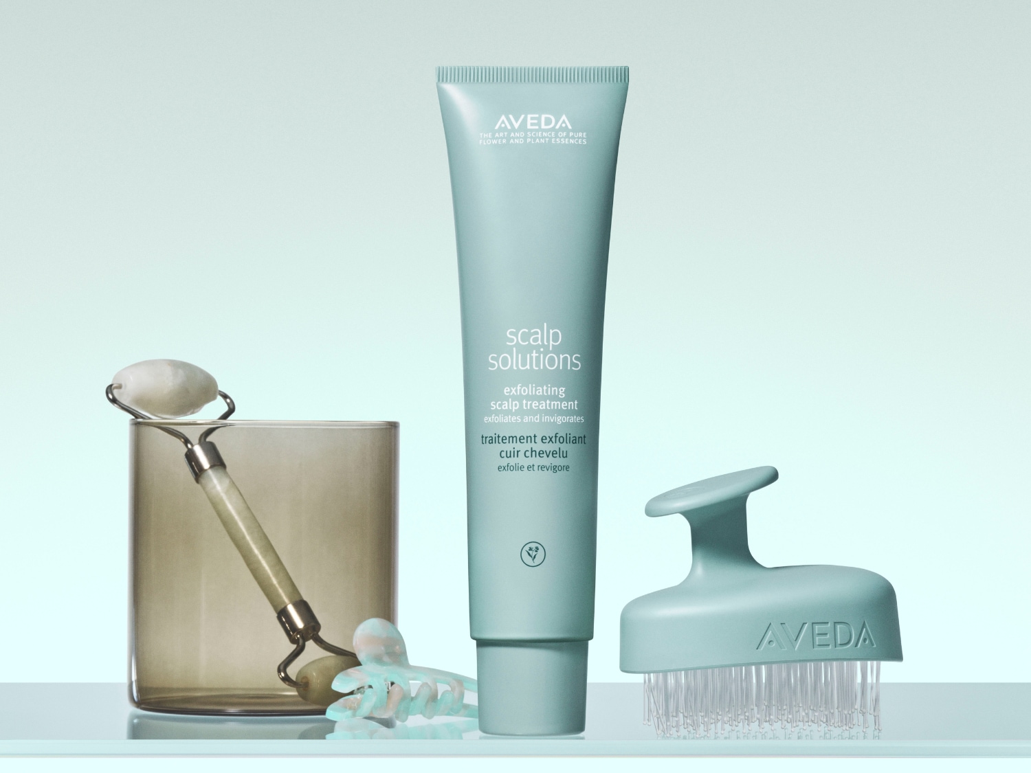 Aveda Scalp Solutions exfoliërende hoofdhuidbehandeling in een blauwgroene tube, samen met een hoofdhuidborstel en een gezichtsroller.