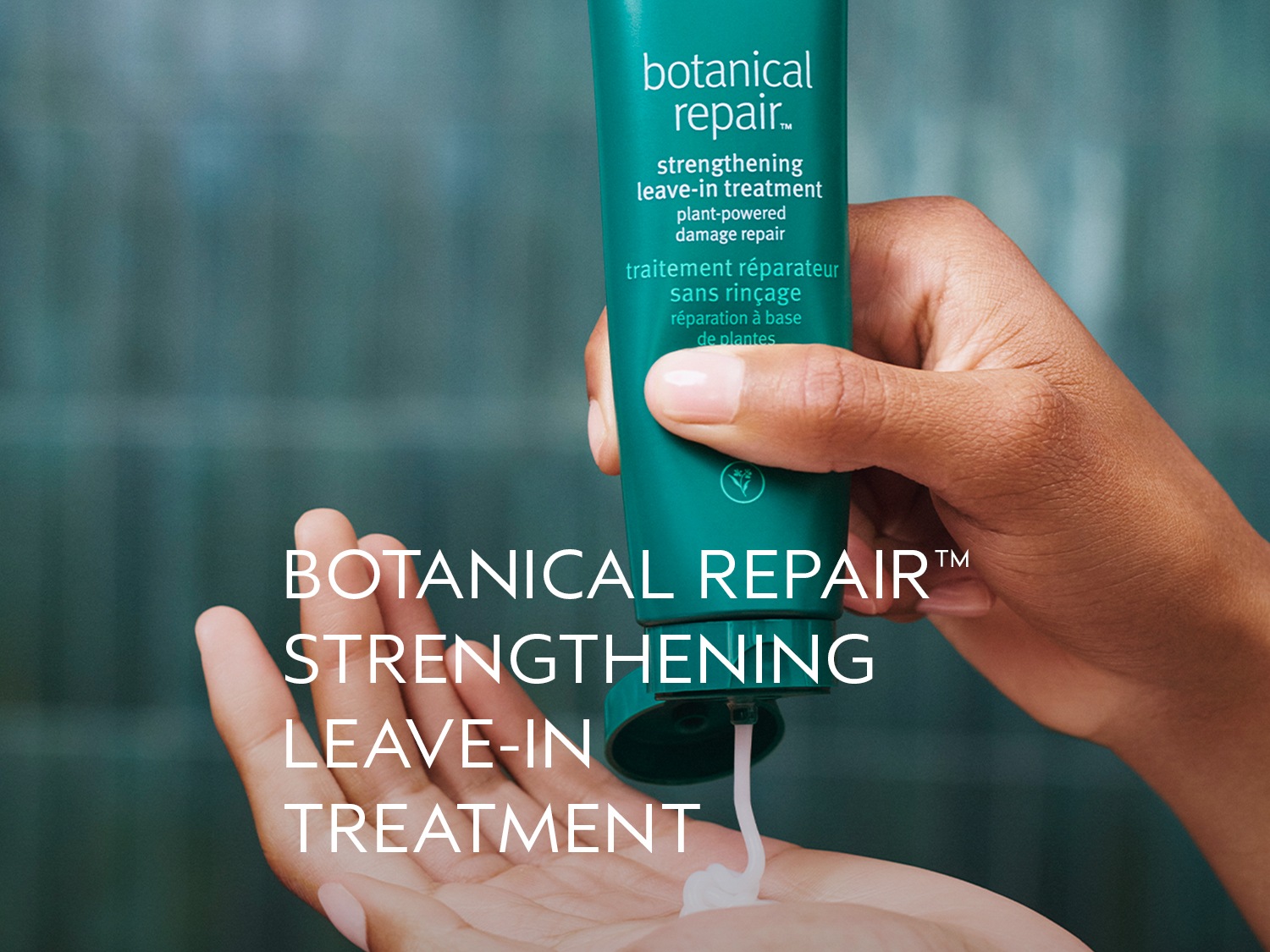 Een hand houdt een groene tube Botanical Repair™ Strengthening Leave-In Treatment vast, terwijl er een witte crème op de handpalm wordt gedrukt.