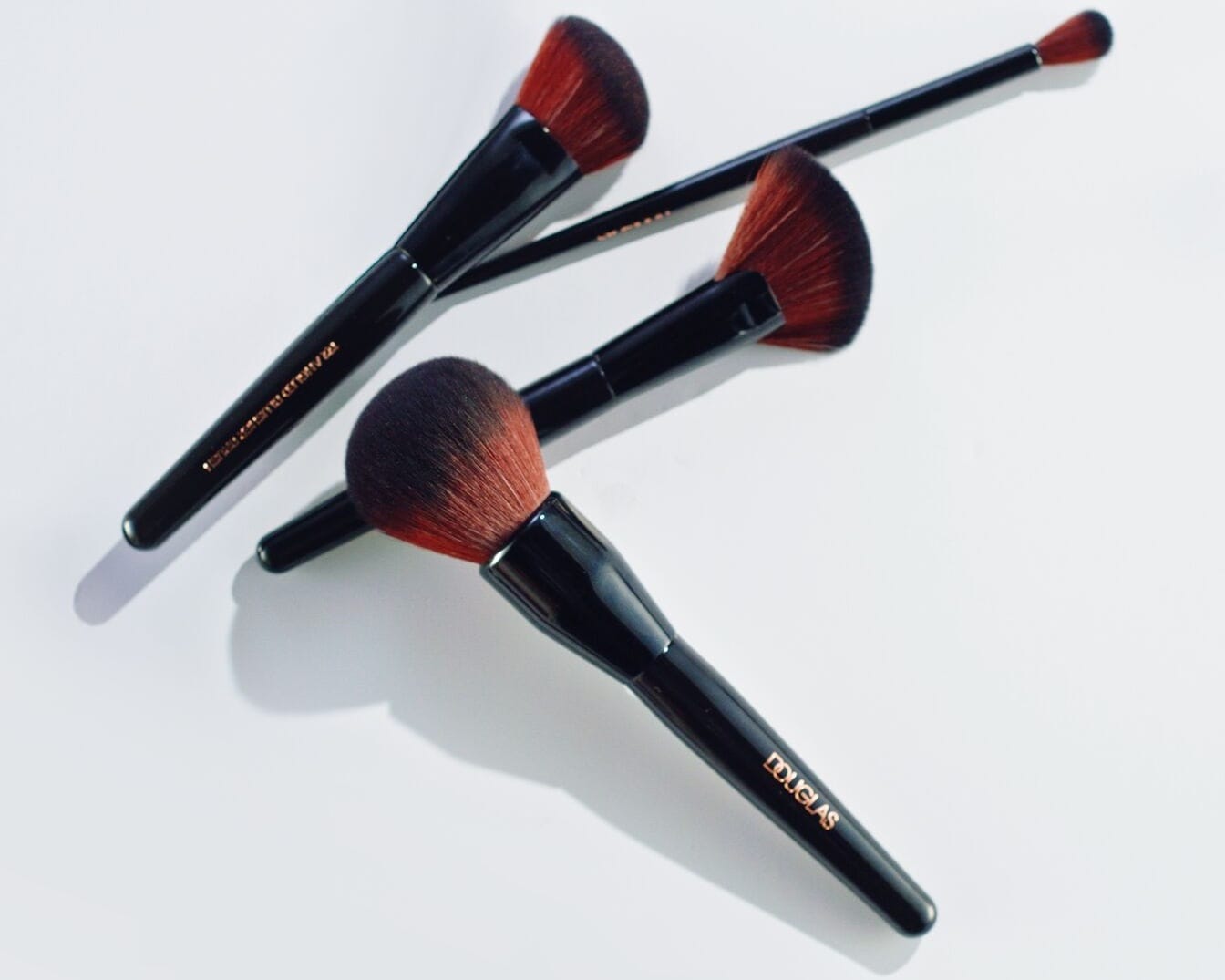 Nahaufnahme von Douglas Make-up Pinselset mit schwarzen Griffen und roten Borsten in verschiedenen Formen und Größen.