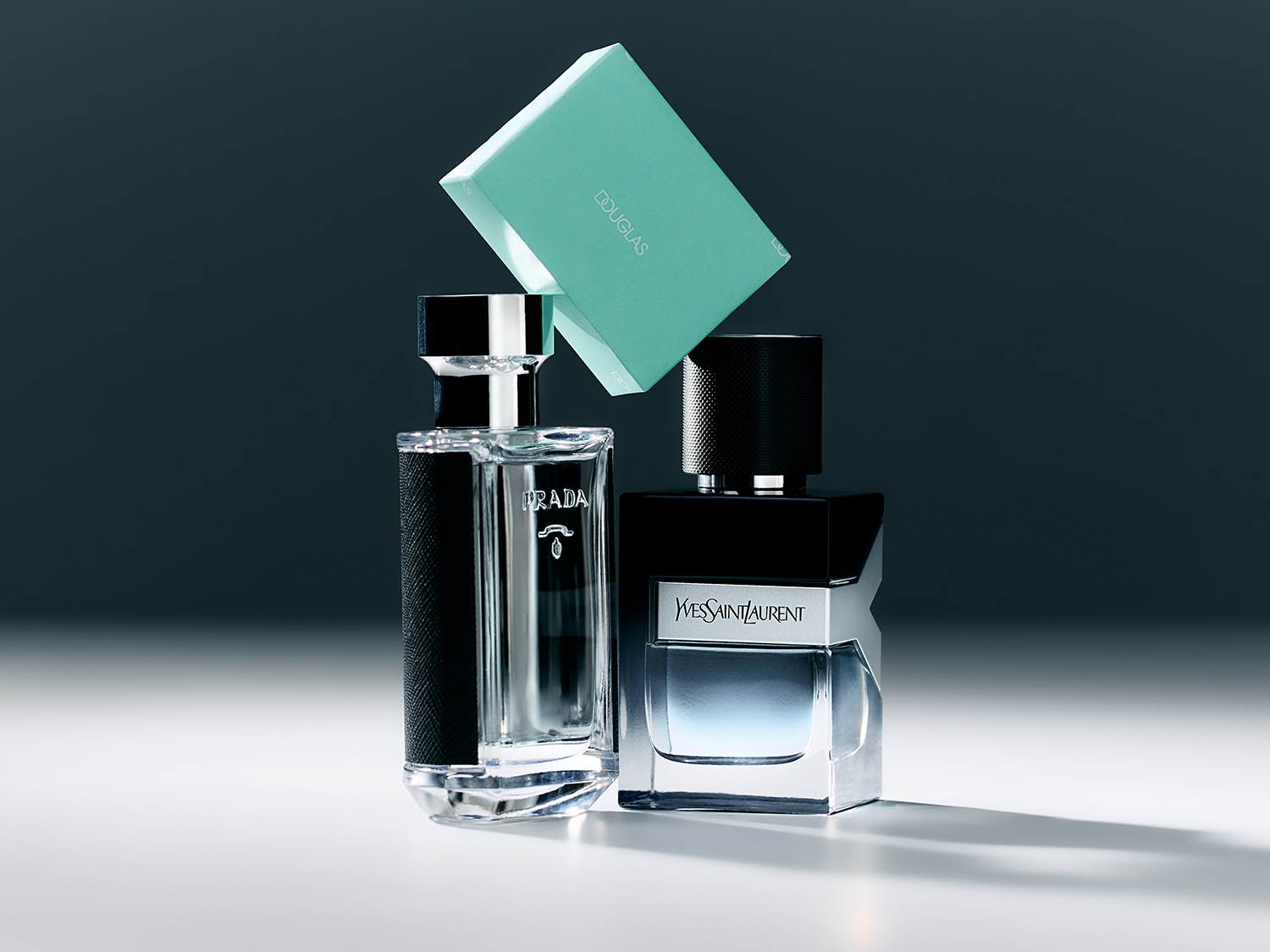 Découvrez l'élégance avec les parfums Prada et Yves Saint Laurent, présentés avec une boîte Douglas turquoise pour une touche de luxe.