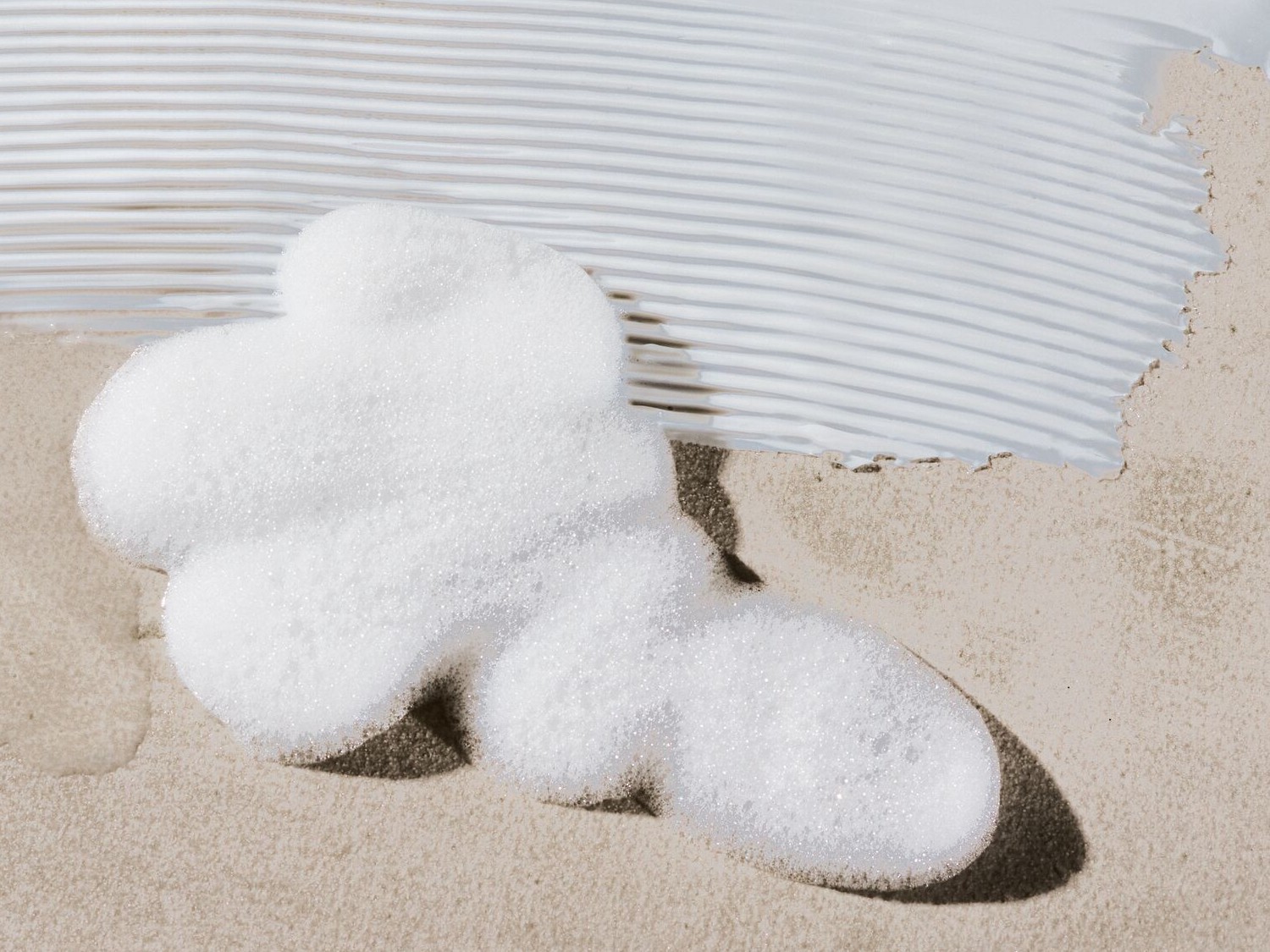 Nahaufnahme von weißem Schaum und einem Streifen weißer Creme auf beigem Untergrund, der die Textur und Anwendung des Produkts hervorhebt.