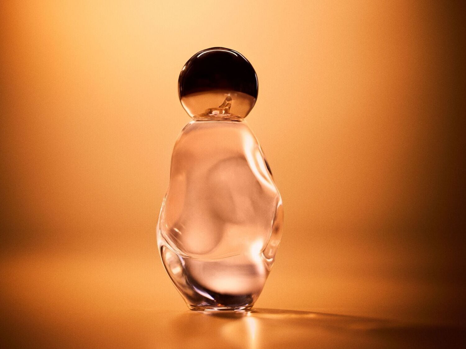 Aukso fone pavaizduotas skaidraus stiklo kvepalų buteliukas su apvaliu juodu dangteliu, elegantiškas aromatas ypatingai progai.