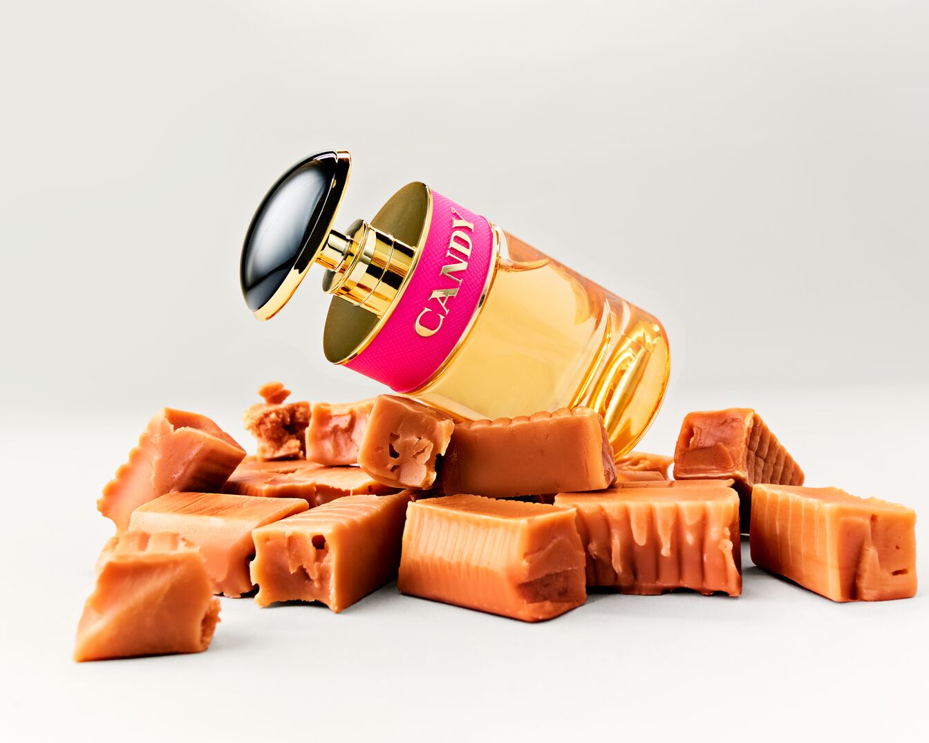 Geltonas „Candy“ aromato buteliukas su rožine etikete guli ant karamelinių saldainių krūvos.