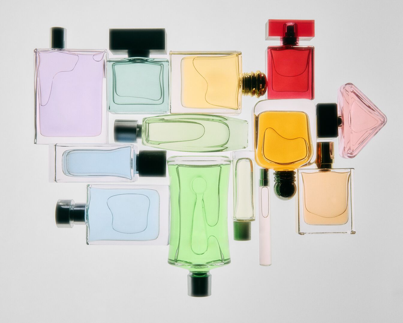 Įvairių spalvų kvepalų buteliukų kolekcija, įskaitant violetinę, žalią, geltoną, raudoną ir mėlyną, išdėstytų ant balto paviršiaus.
