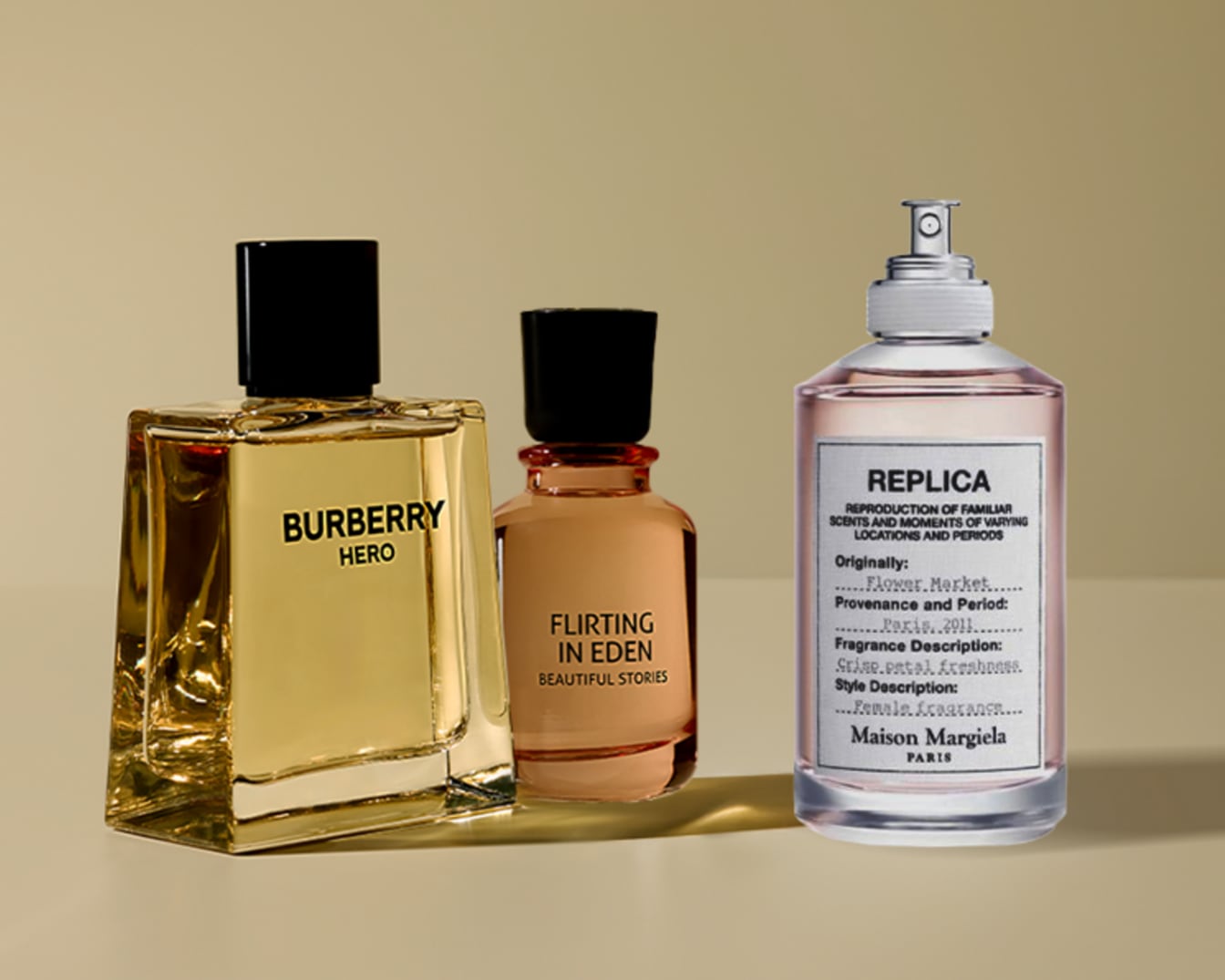 Trys skirtingi kvepalų buteliukai: „Burberry Hero“ su juodu dangteliu ir auksiniais kvepalais, „Flirting in Eden“ su juodu dangteliu ir rausvais kvepalais bei „Maison Margiela Replica“ su sidabriniu dangteliu ir rausvais kvepalais.