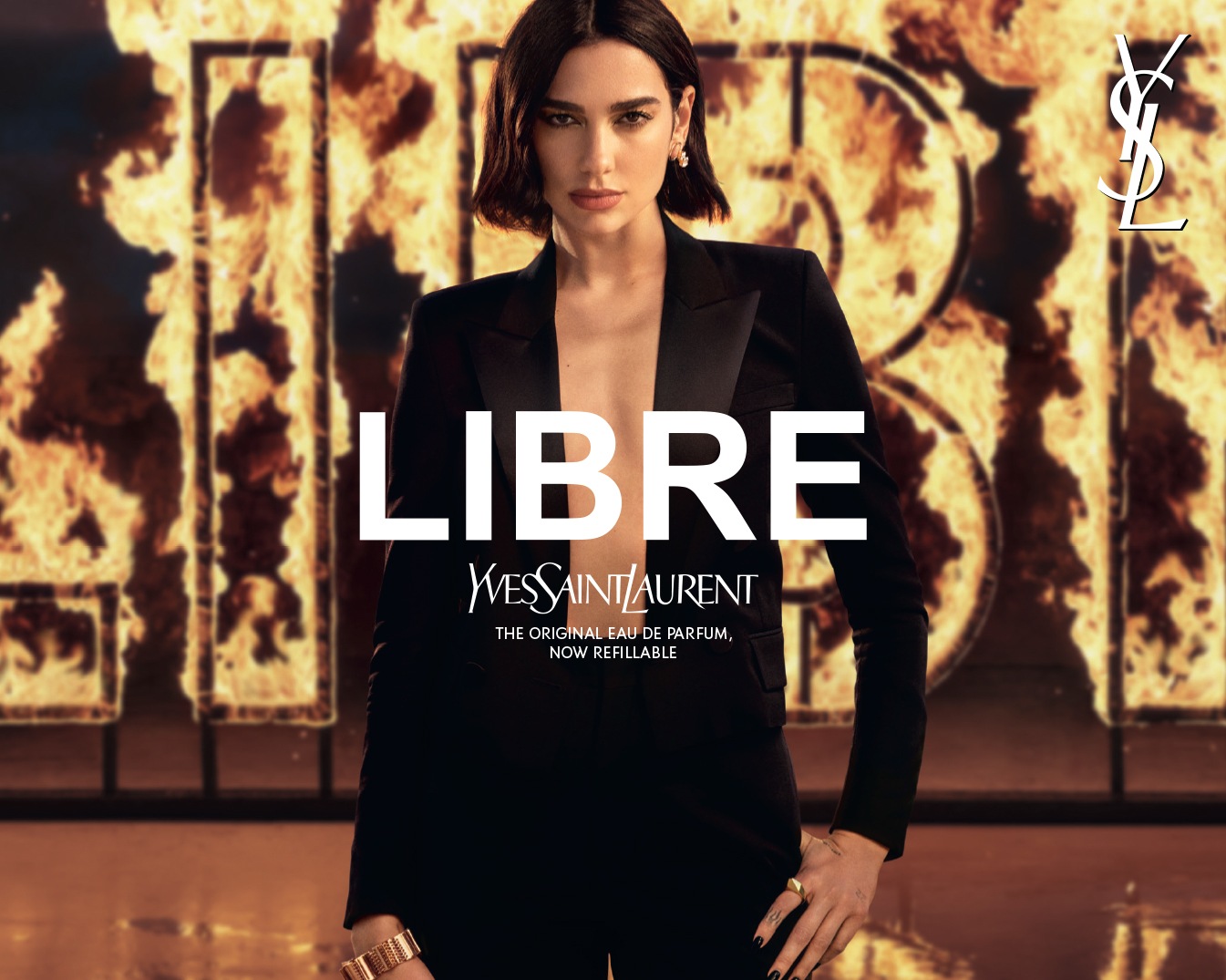 Découvrez Libre d'Yves Saint Laurent, l'eau de parfum originale désormais rechargeable, incarnée par une femme élégante en tailleur noir devant un fond enflammé.
