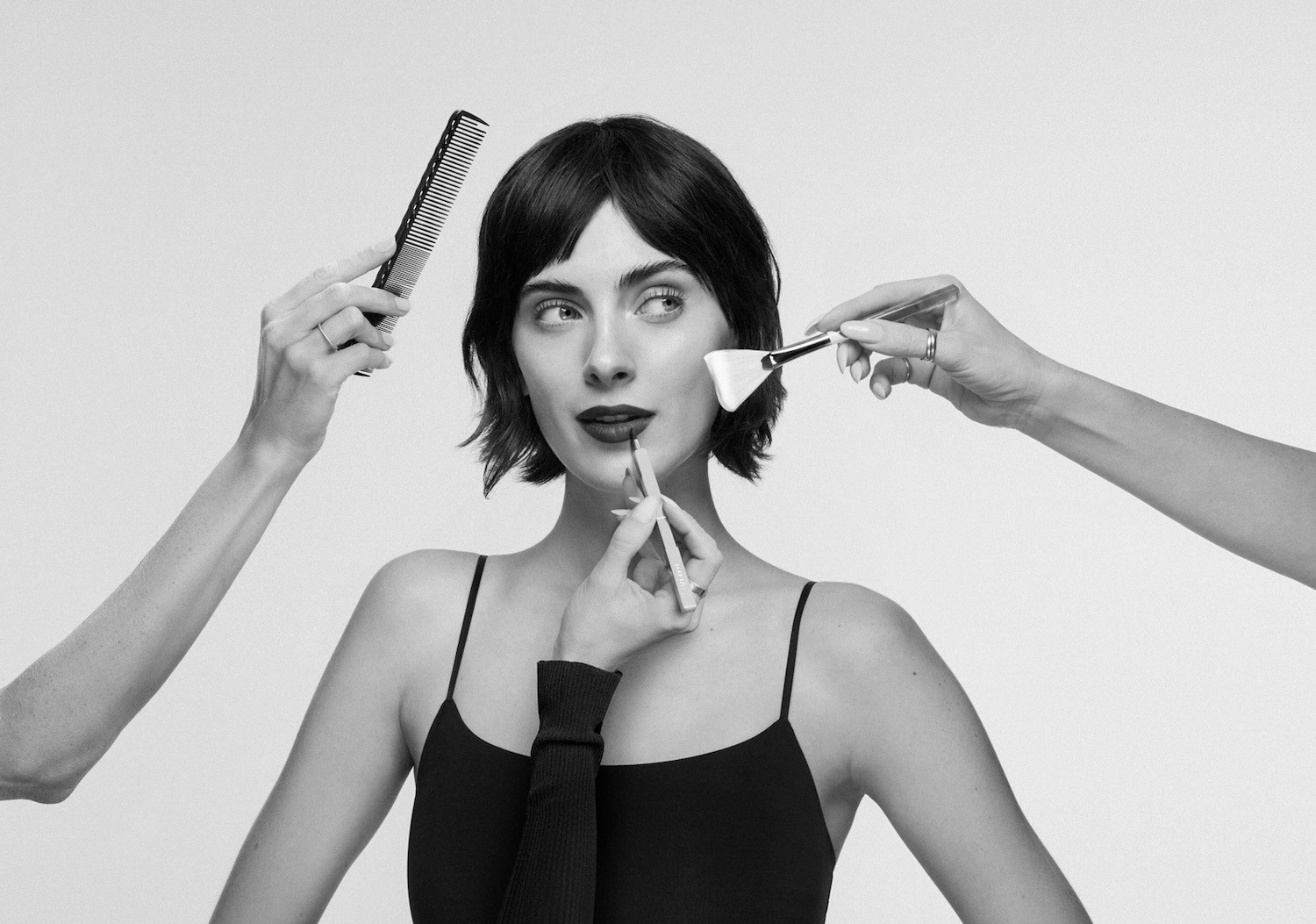 Primo piano in bianco e nero di una donna che si trucca con un pennello per il viso, una matita per le labbra e un pettine per capelli.