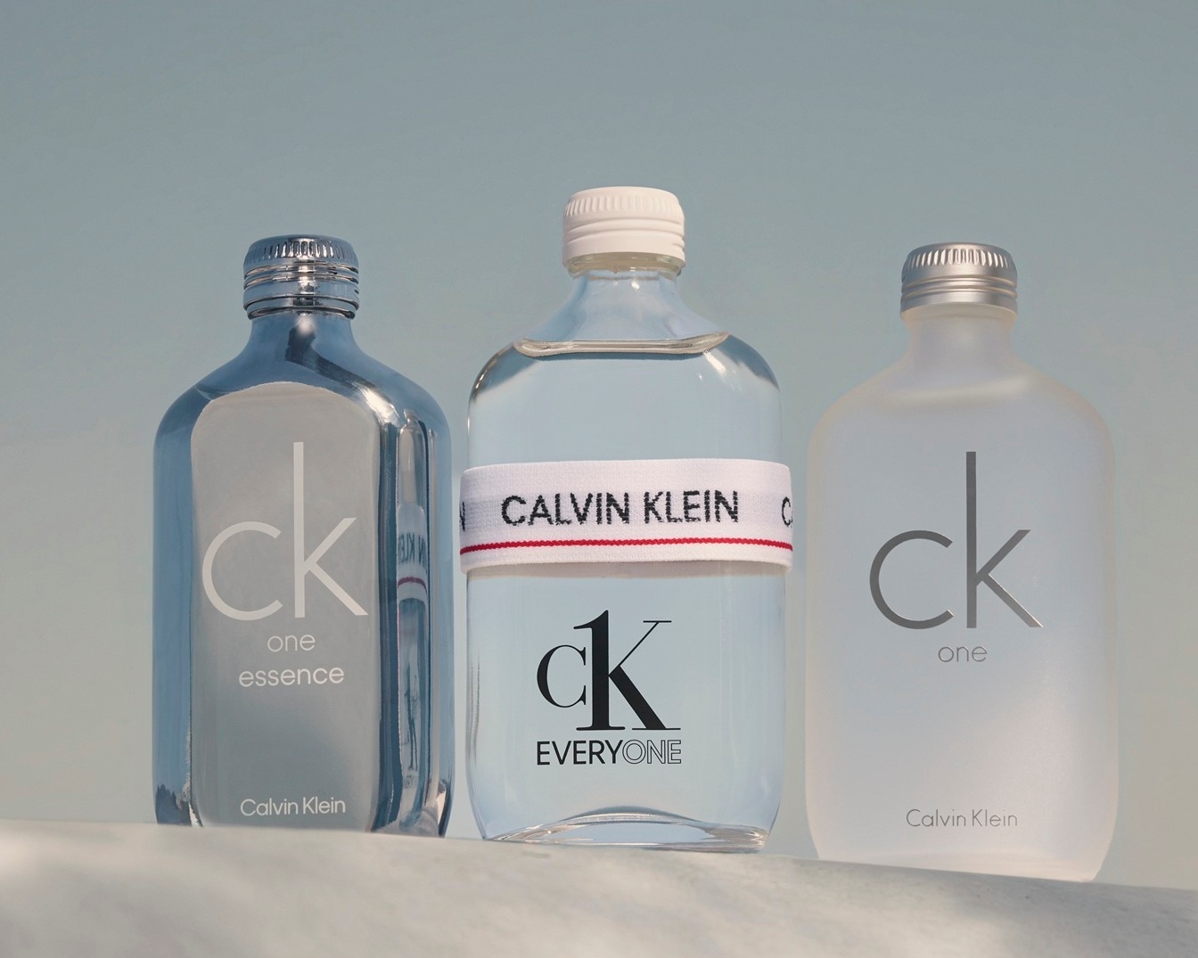Ecco tre flaconi di profumo Calvin Klein: CK One Essence in una bottiglia blu metallizzato, CK Everyone con una fascia bianca con logo e CK One in vetro smerigliato.