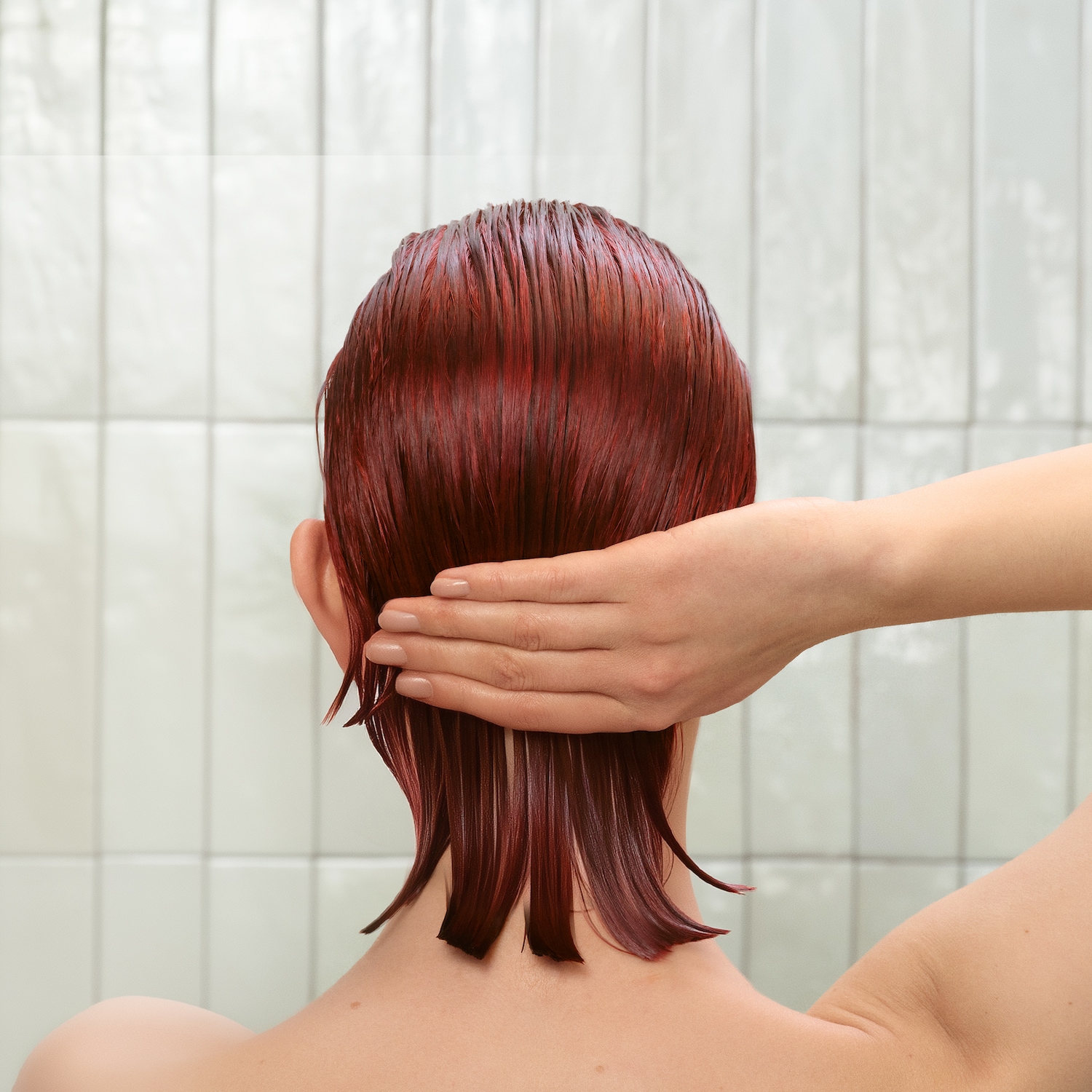 Vista posteriore di una donna con i capelli rosso mogano umidi, mentre una mano le tocca delicatamente la nuca.