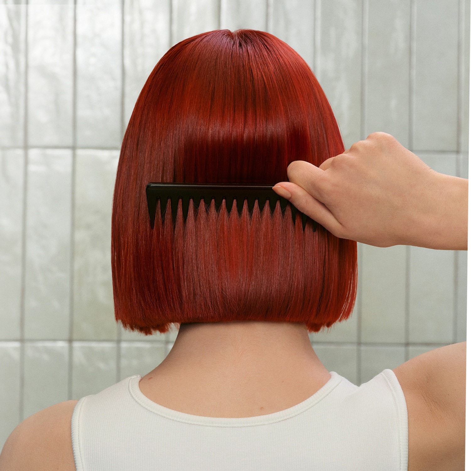 Vista posteriore di una donna che si pettina i capelli rossi con un pettine nero, mostrando una chioma liscia e curata.