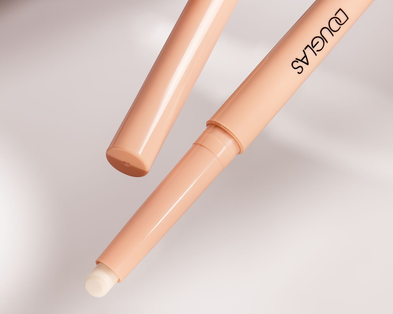 Close-up van een Douglas concealer stick met een perzikkleurige verpakking en een crèmekleurige punt.