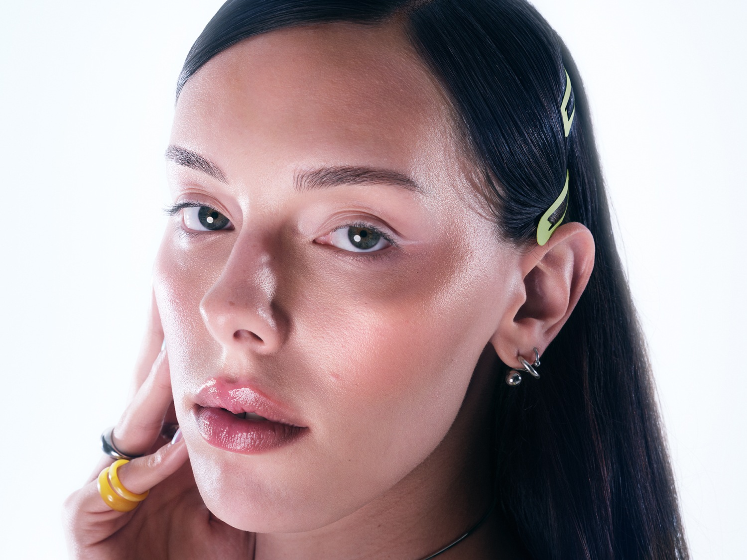 Gros plan sur le visage d'une femme aux cheveux noirs brillants, agrémentés de barrettes vert clair, avec un maquillage subtil mettant en valeur ses lèvres brillantes et ses yeux expressifs.