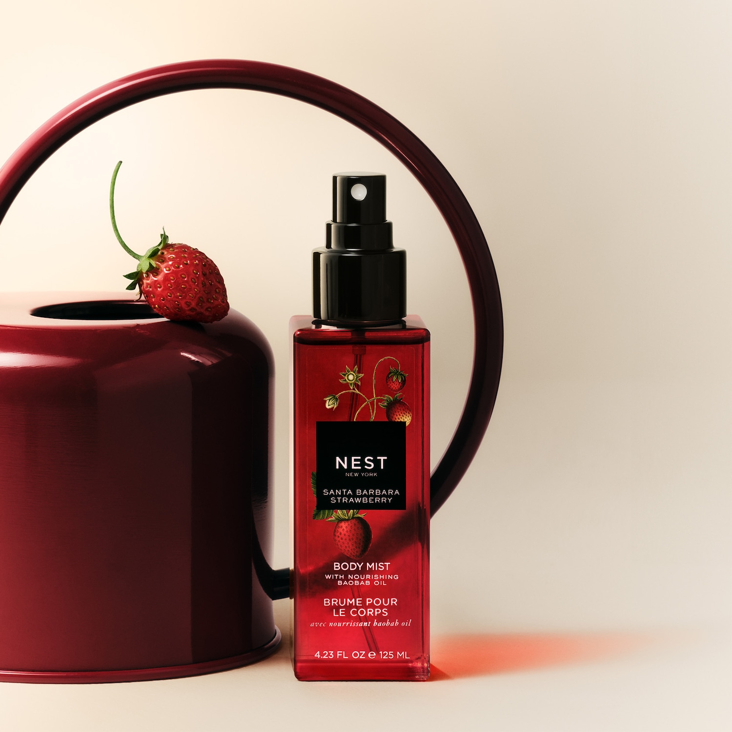 A Nest New York Santa Barbara Strawberry testpermet piros üvegben, fekete kupakkal, mellette egy piros eperrel díszített piros vázával.