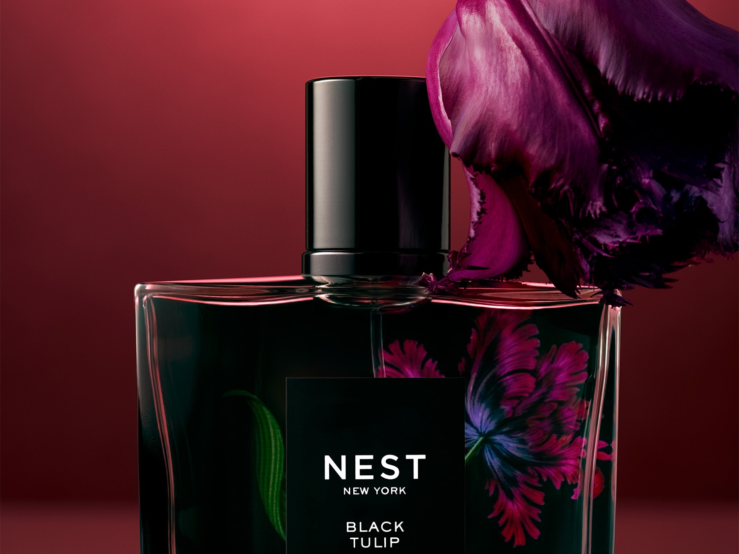 A Nest New York Black Tulip parfümös üvege látható, melyet egy lila tulipán díszít, elegáns és kifinomult megjelenést kölcsönözve.