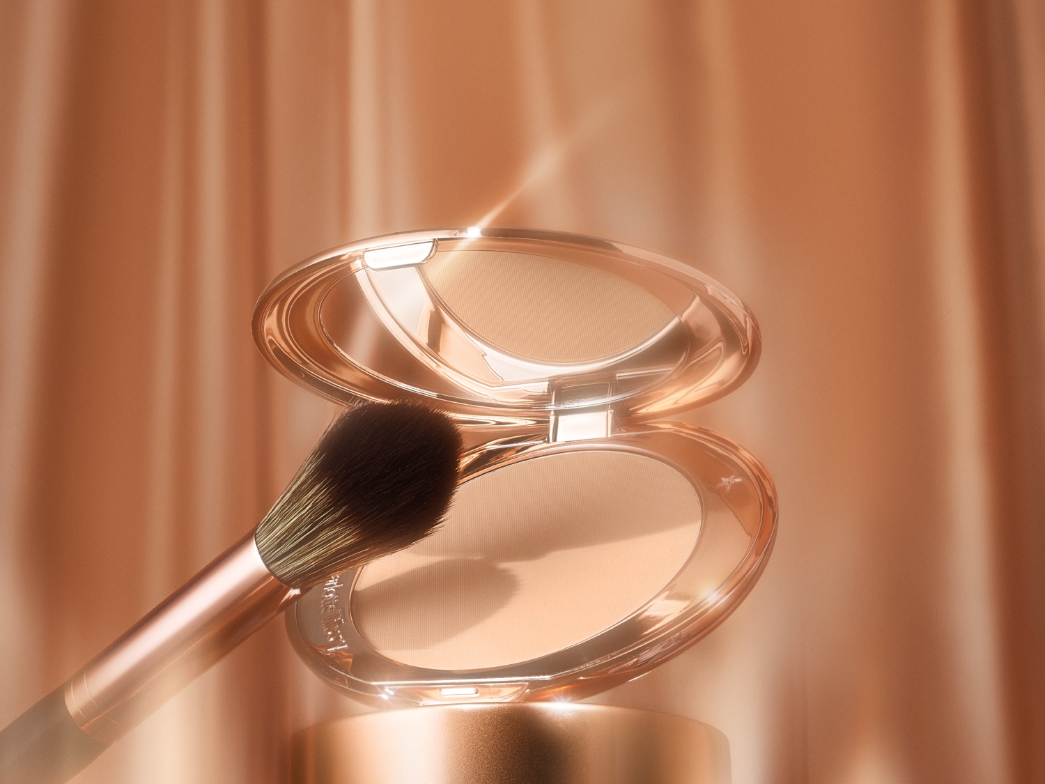 Nahaufnahme eines offenen, goldenen Make-up-Puders mit einem Pinsel, der auf dem Puder liegt, vor einem goldenen Hintergrund.