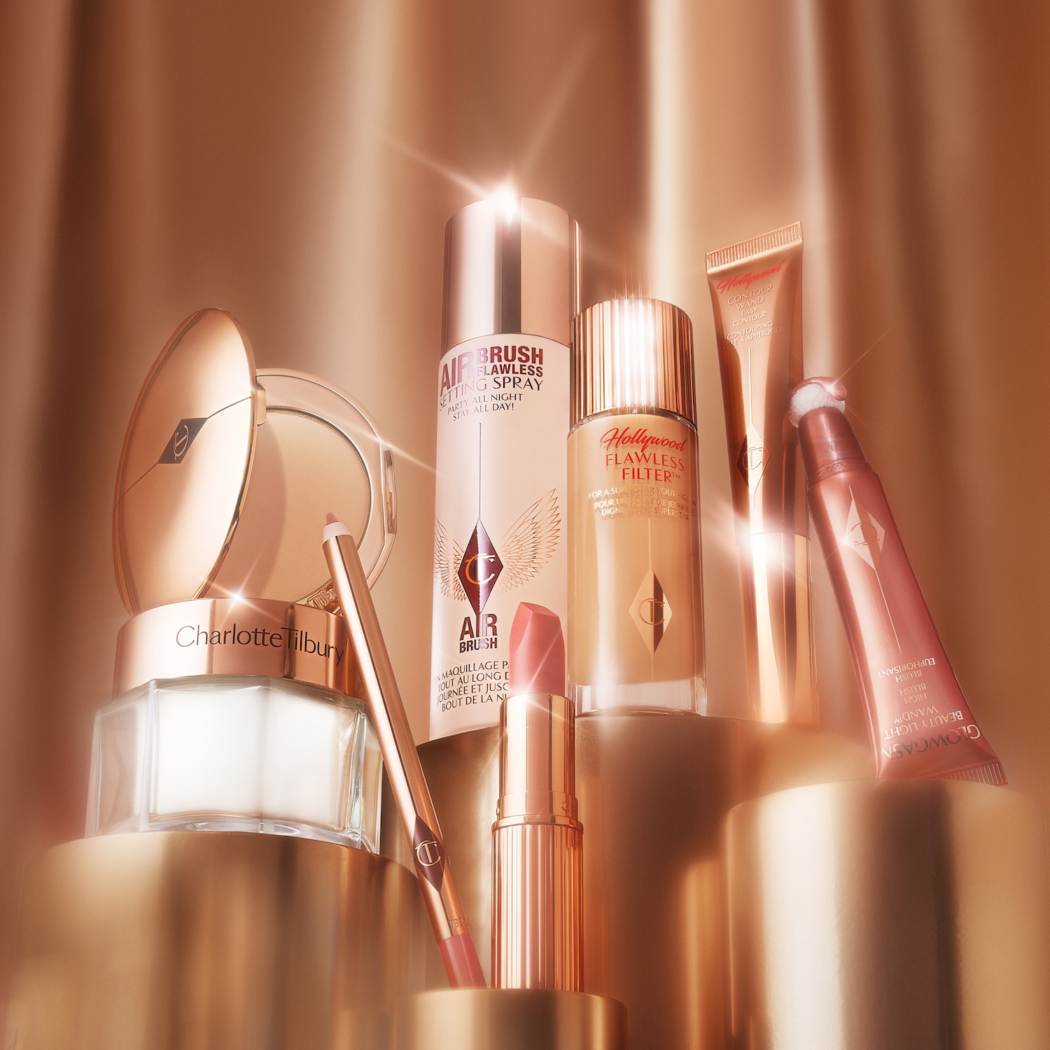 Eine Sammlung von Charlotte Tilbury Make-up-Produkten in Goldtönen, darunter Airbrush Setting Spray, Hollywood Flawless Filter und Glowgasm Beauty Light Wand.