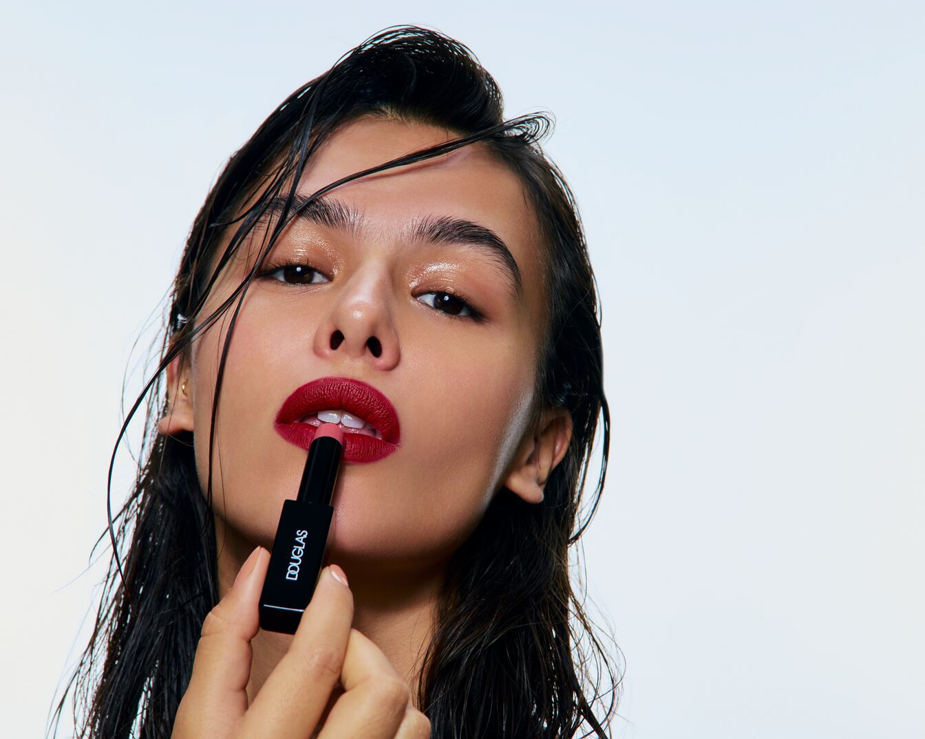 Een vrouw met nat haar brengt rode lippenstift aan uit een zwarte Douglas lippenstift huls.
