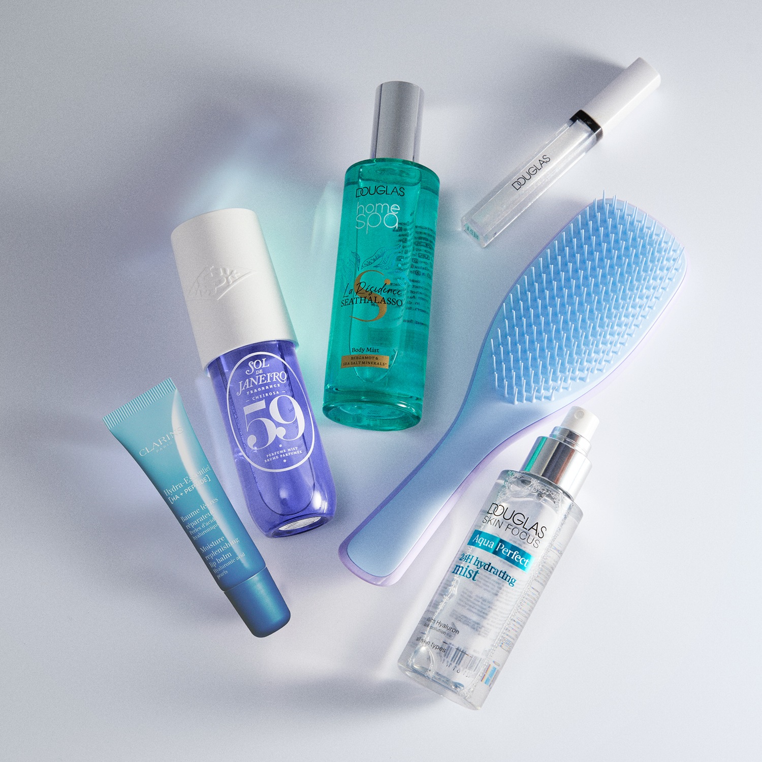 Een verzameling schoonheidsproducten, waaronder Clarins lippenbalsem, Sol de Janeiro parfum, Douglas Home Spa body mist, een haarborstel en Douglas Skin Focus hydraterende mist.