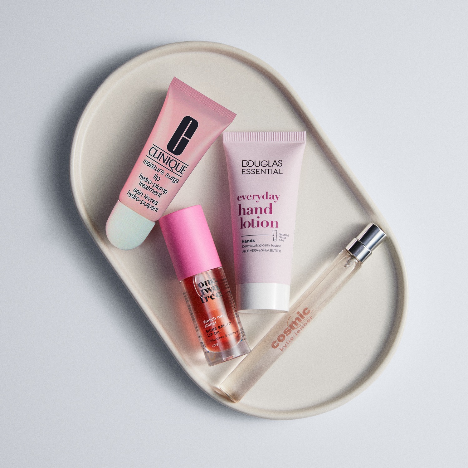 Ontdek een verzameling van huidverzorgingsproducten, waaronder Clinique lipbehandeling, Douglas handlotion, One Two Free lipolie en Cosmic Kylie Jenner parfum, gepresenteerd op een elegante crèmekleurige achtergrond.