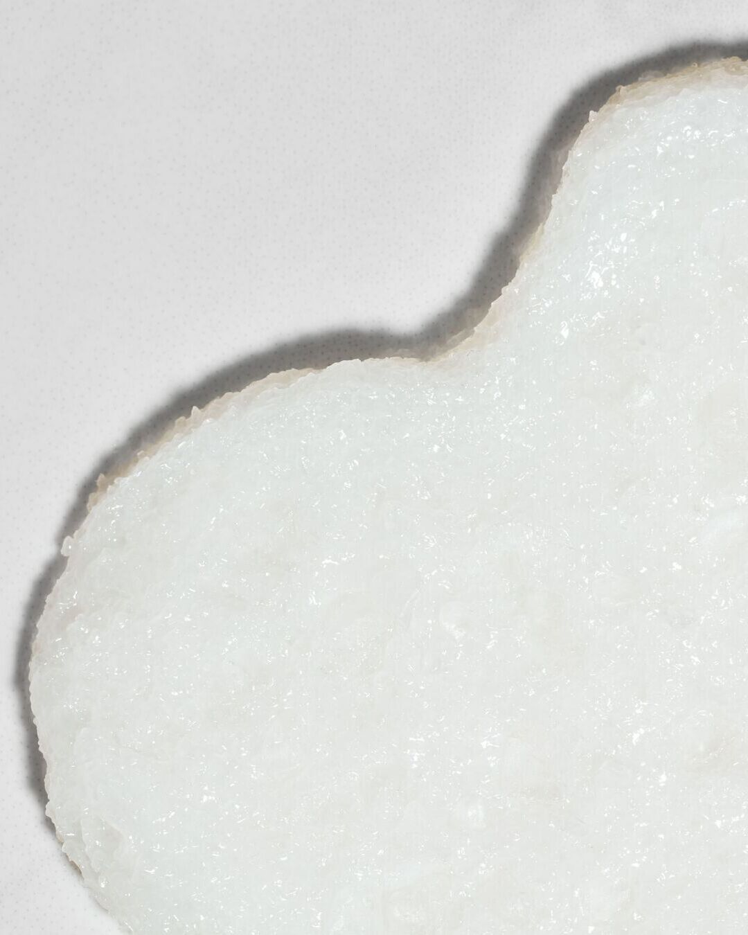 Baltas veido kaukės lakštas ant balto paviršiaus, skirtas odos priežiūrai ir drėkinimui.