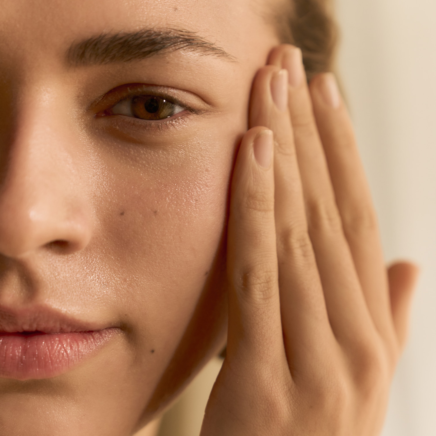 Nahaufnahme einer Frau, die eine Hand auf ihre strahlende Haut legt, um die feuchtigkeitsspendende Wirkung einer neuen Hautpflegeroutine zu demonstrieren.