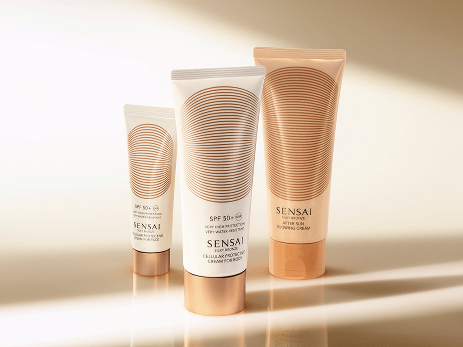 Drei Tuben Sensai Sonnenschutzprodukte in verschiedenen Größen, von Gesichtscreme bis After-Sun-Lotion, alle mit elegantem, bronzefarbenem Design.