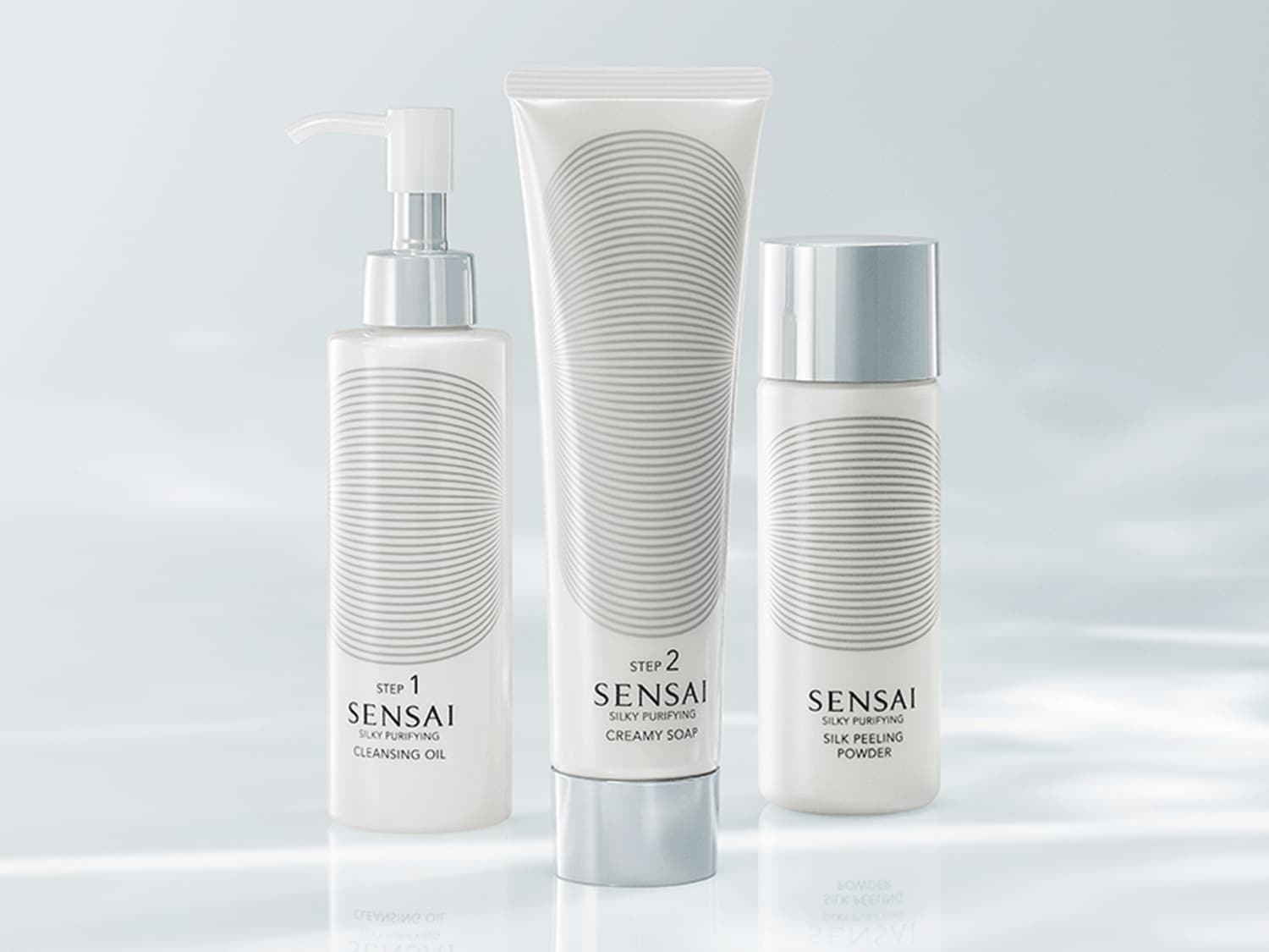 Drei weiße Sensai-Hautpflegeprodukte mit silbernen Akzenten, darunter Reinigungsöl, cremige Seife und Seidenpeeling-Puder, die für eine seidige Reinigung sorgen.