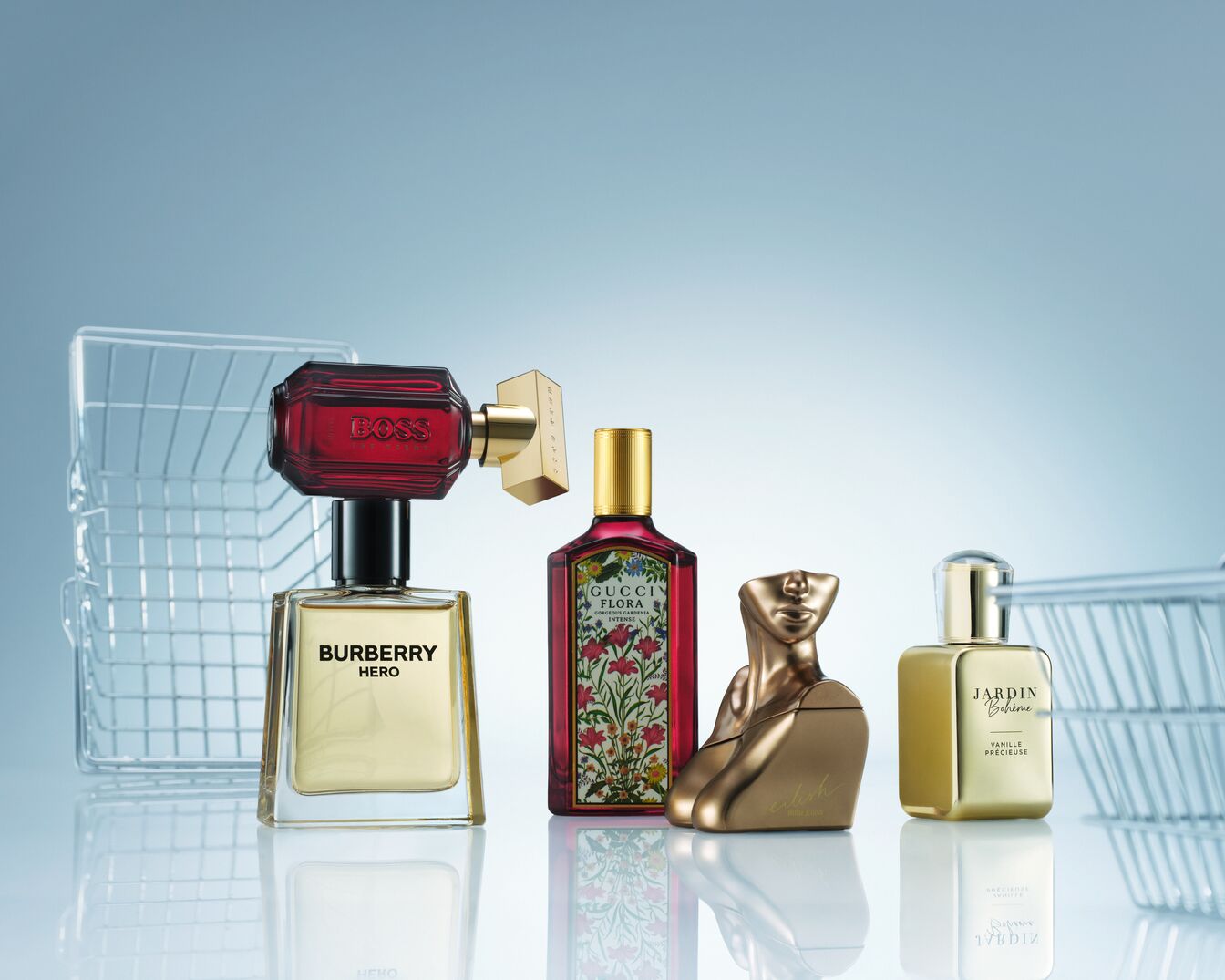A képen négy különböző parfüm látható, köztük a Burberry Hero, a Gucci Flora, egy arany színű, női testet formázó üveg, és a Jardin Bohème Vanille Précieuse, mindegyik egy-egy bevásárlókosár mellett.
