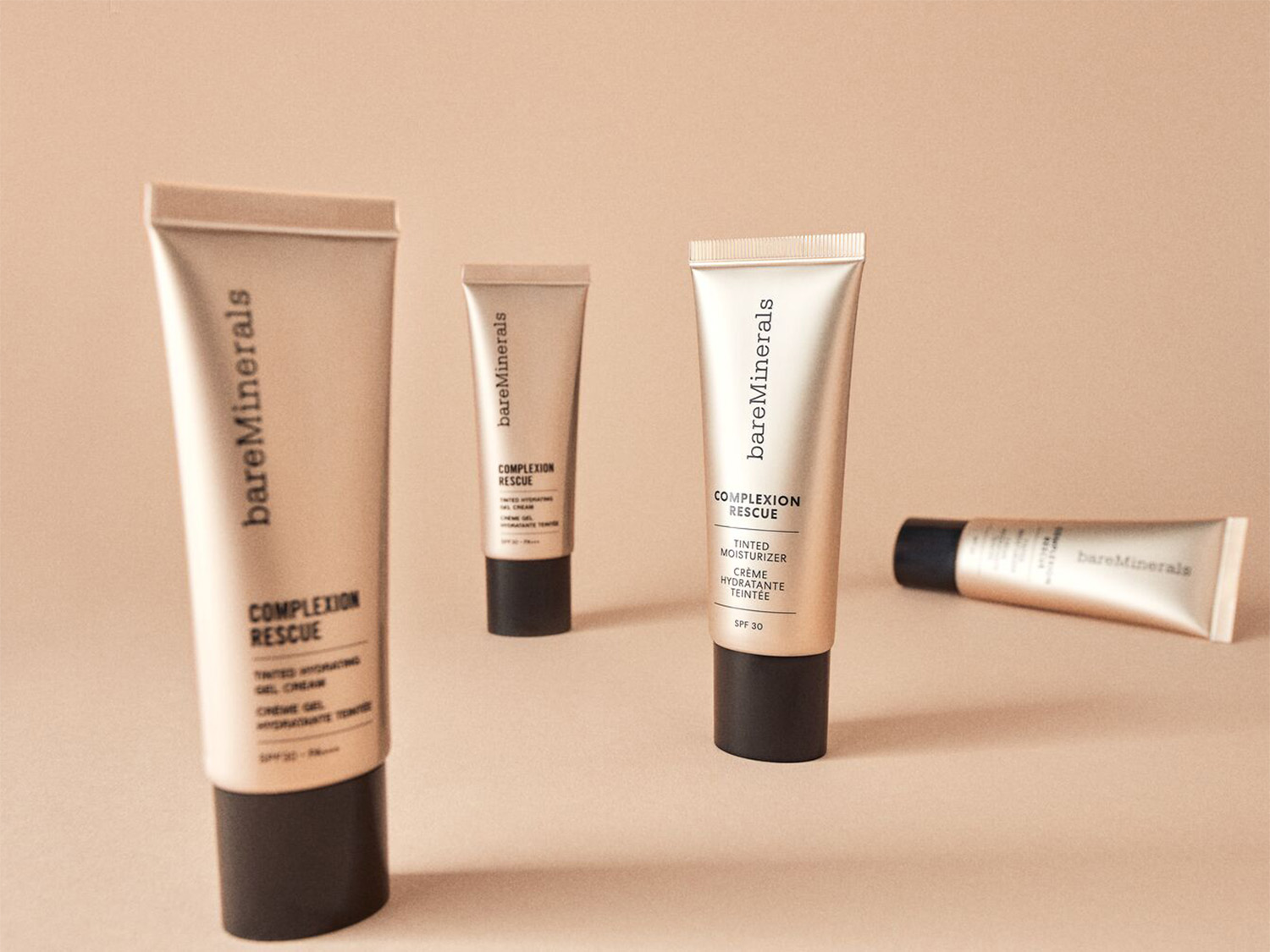 Verschillende tubes BareMinerals Complexion Rescue, een getinte hydraterende gelcrème met SPF 30, staan op een beige achtergrond.