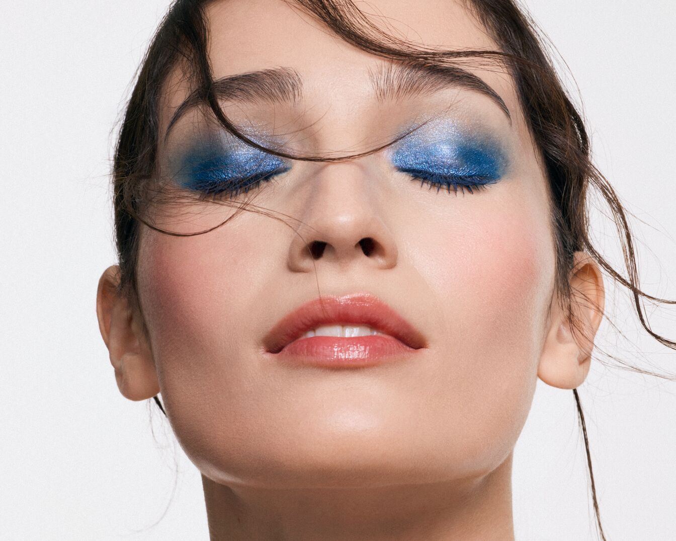 Nahaufnahme eines Frauengesichts mit schimmerndem, blauem Lidschatten und glänzenden Lippen, die einen strahlenden und modernen Look erzeugen.