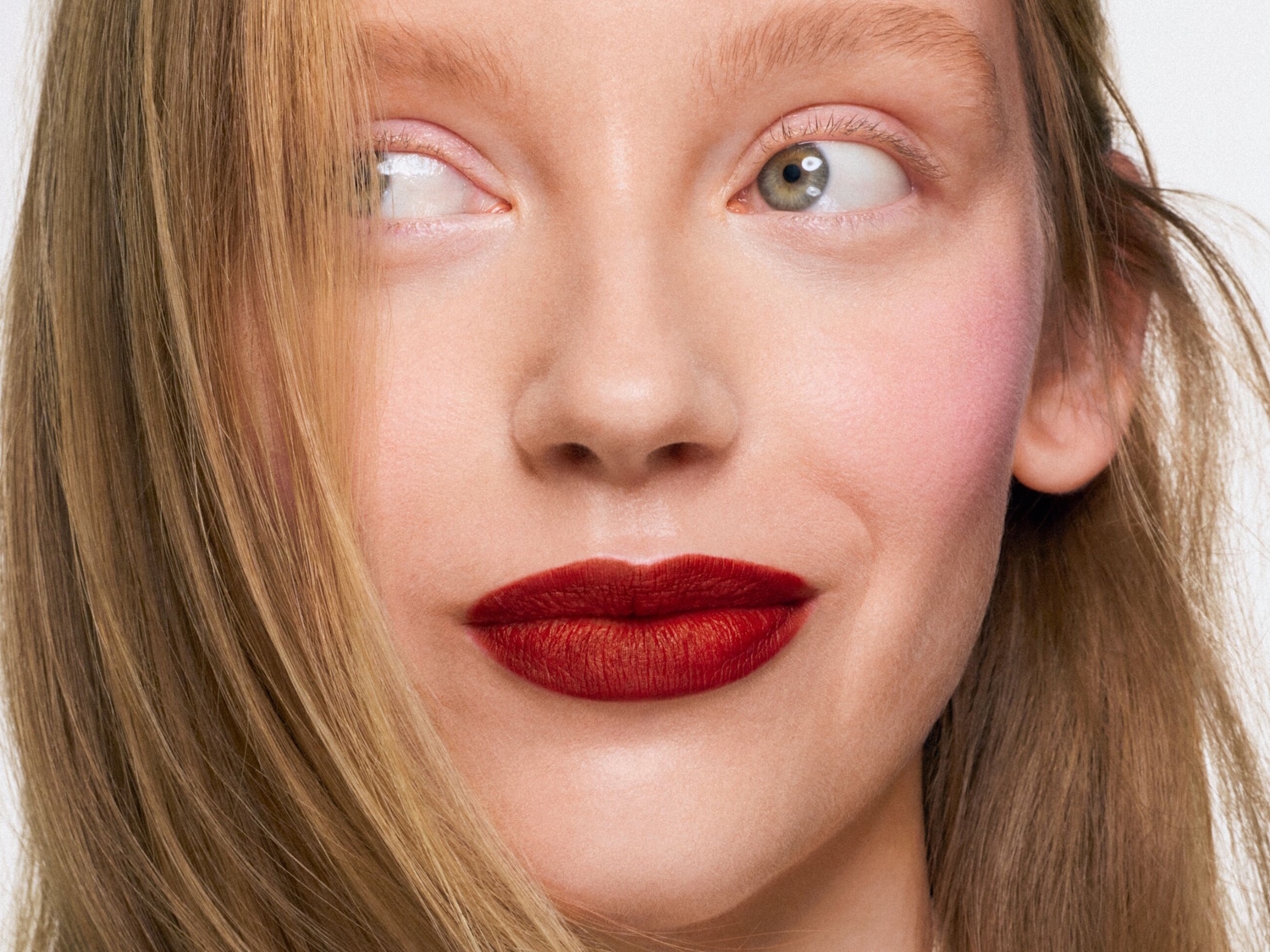 Nahaufnahme eines Frauengesichts mit roten Lippen, rosigen Wangen und blonden Haaren, die ihr Gesicht teilweise bedecken.