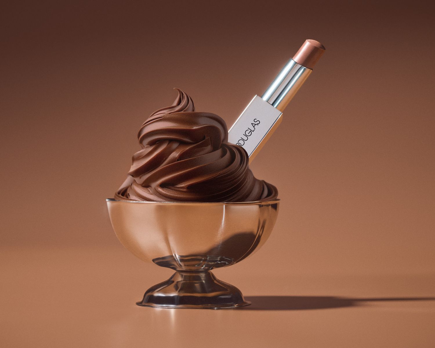 Ein bronzefarbener Lippenstift von Douglas steckt in einem silbernen Eisbecher, der mit einer Schokoladencreme gefüllt ist, alles vor einem braunen Hintergrund.