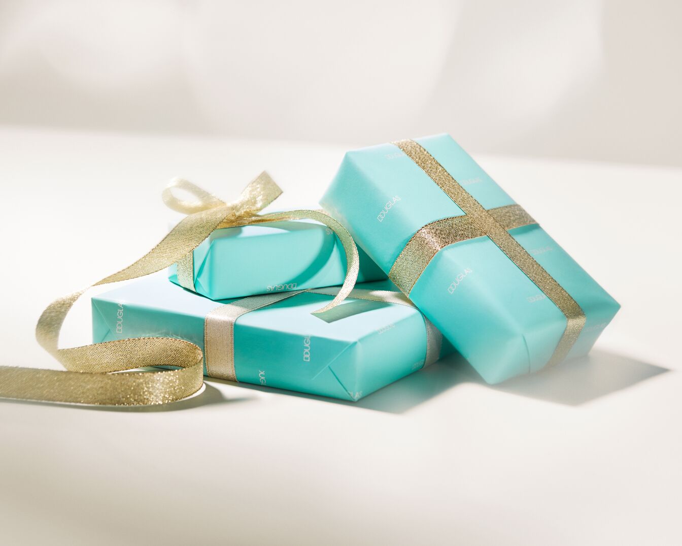 Ein Stapel aus drei hellblau verpackten Douglas Geschenken, verziert mit goldenen Bändern und Schleifen, die Eleganz und festliche Stimmung vermitteln.