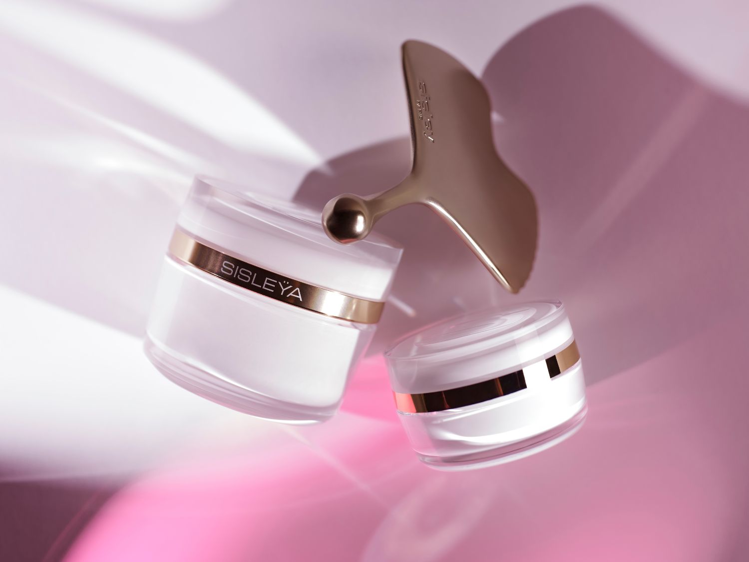 Découvrez le soin Sisleÿa dans son élégant pot blanc et or, accompagné de son outil de massage doré pour une peau éclatante.