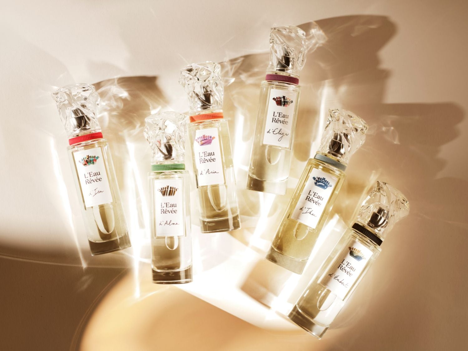 Découvrez L'Eau Rêvée, une collection de parfums aux flacons transparents et aux bouchons en cristal, chacun orné d'une étiquette élégante et d'un détail coloré distinctif.