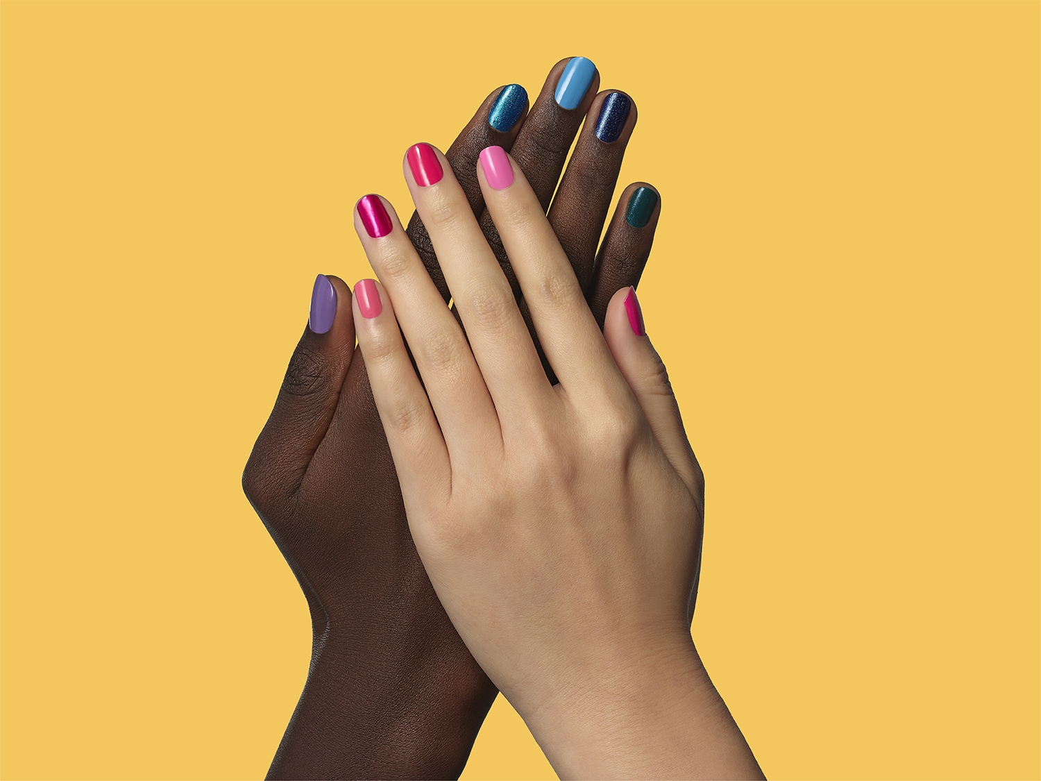 Gros plan sur deux mains de couleurs différentes, les doigts vernis de couleurs vives comme le violet, le rose et le bleu, se touchant sur un fond jaune.