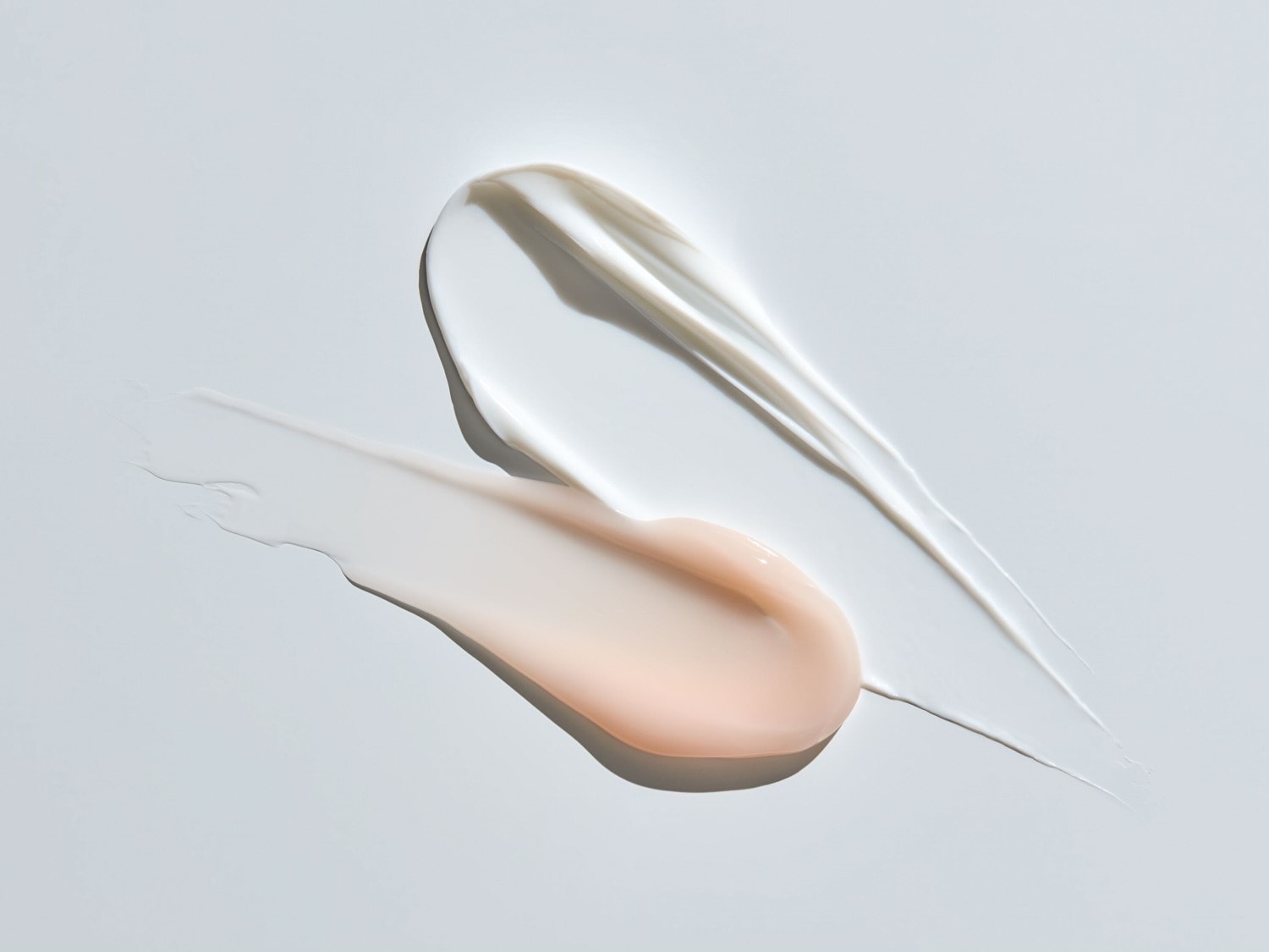 Nahaufnahme von zwei Cremestrichen, einer in Weiß und der andere in einem zarten Pfirsichton, die die Textur und Konsistenz von Schönheitsprodukten hervorheben.