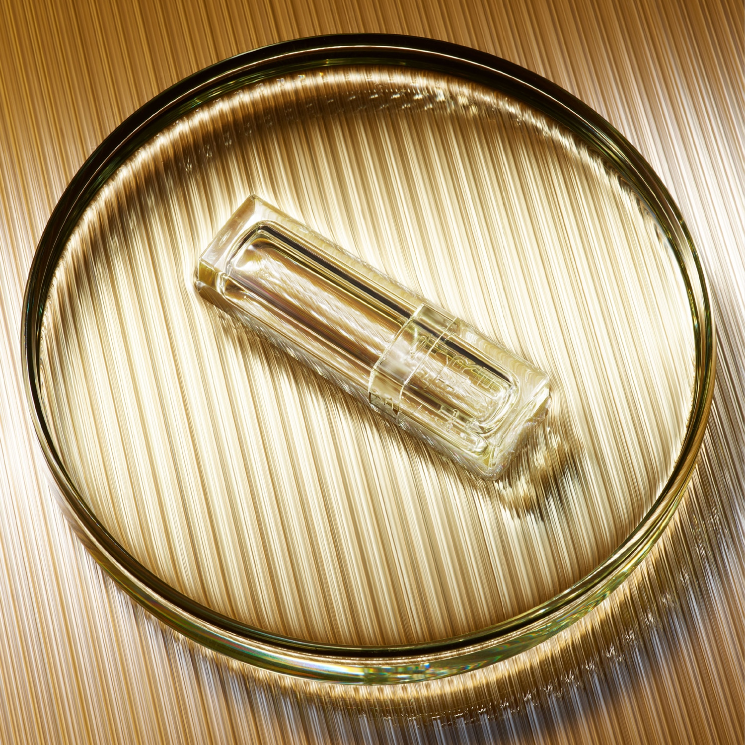 Un flacon de parfum transparent repose sur un plateau doré texturé, capturant la lumière et l'élégance.