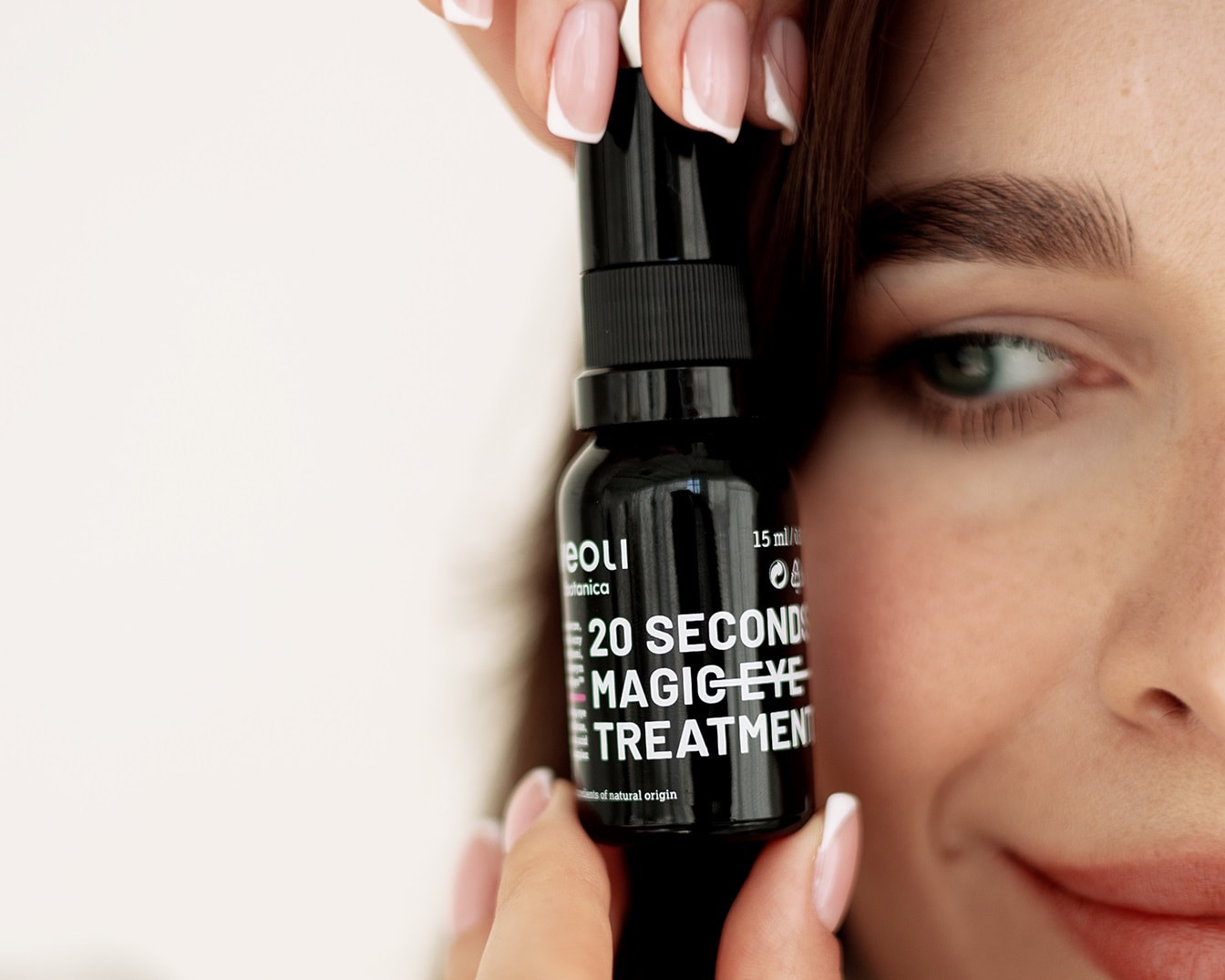 Kobieta trzyma czarną butelkę Eoli Botanica 20 Second Magic Eye Treatment, produktu do pielęgnacji okolic oczu, obok swojej twarzy.