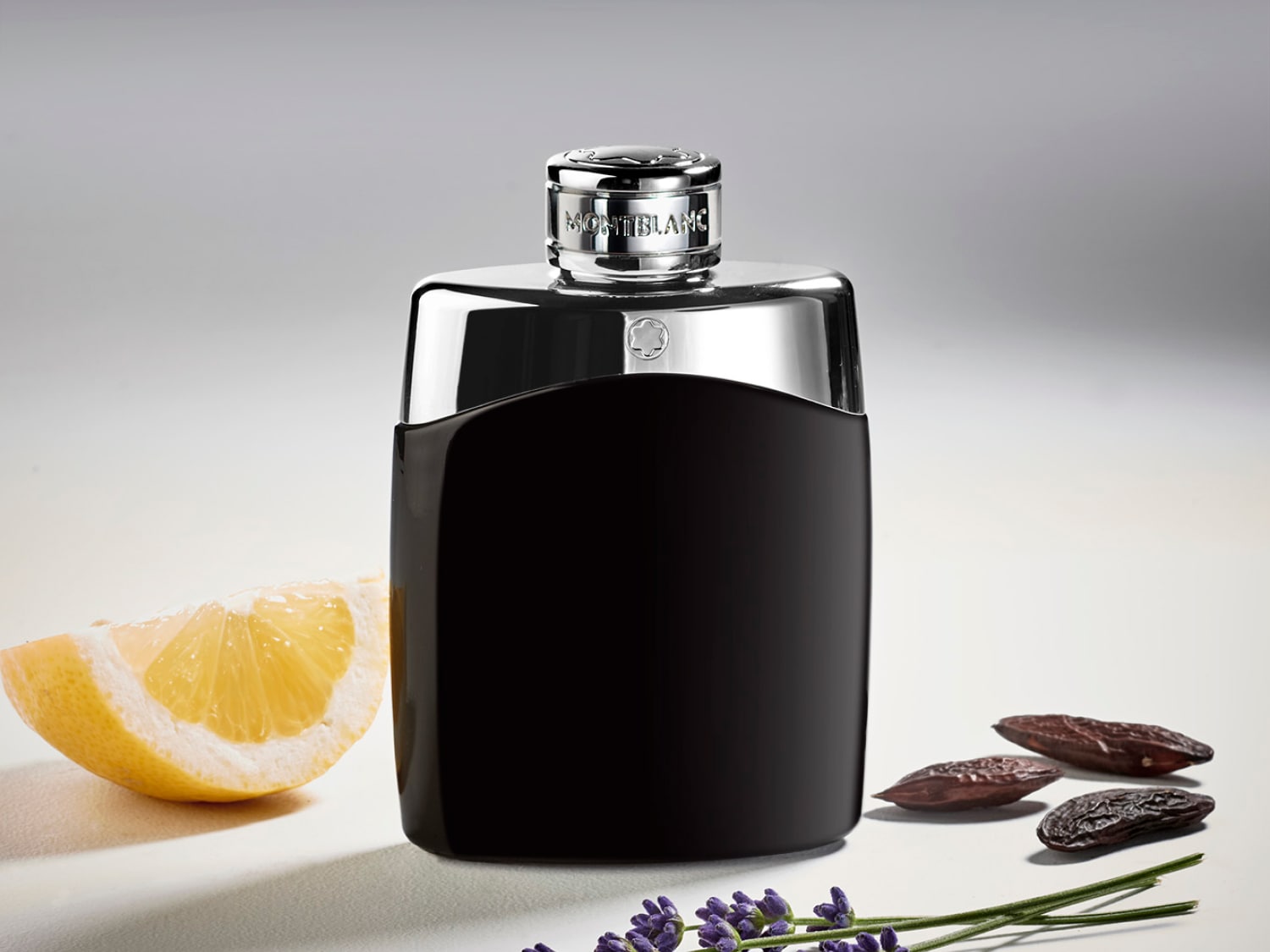 Elegante flacone di profumo Montblanc Legend nero con tappo argentato, adagiato accanto a una fetta di limone, fava tonka e fiori di lavanda.