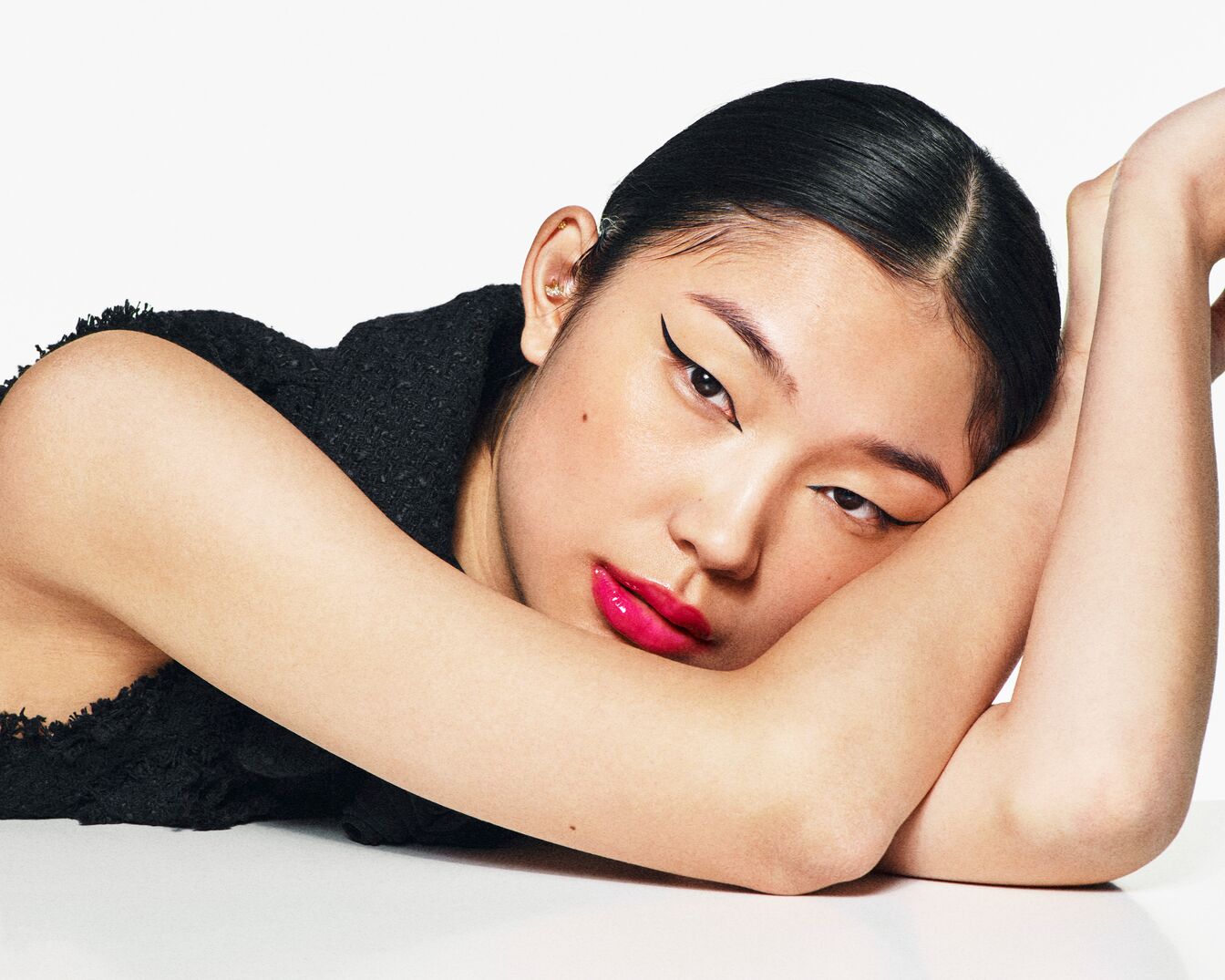 Portret kobiety z czarnym eyelinerem i różową szminką, opierającej się na rękach.