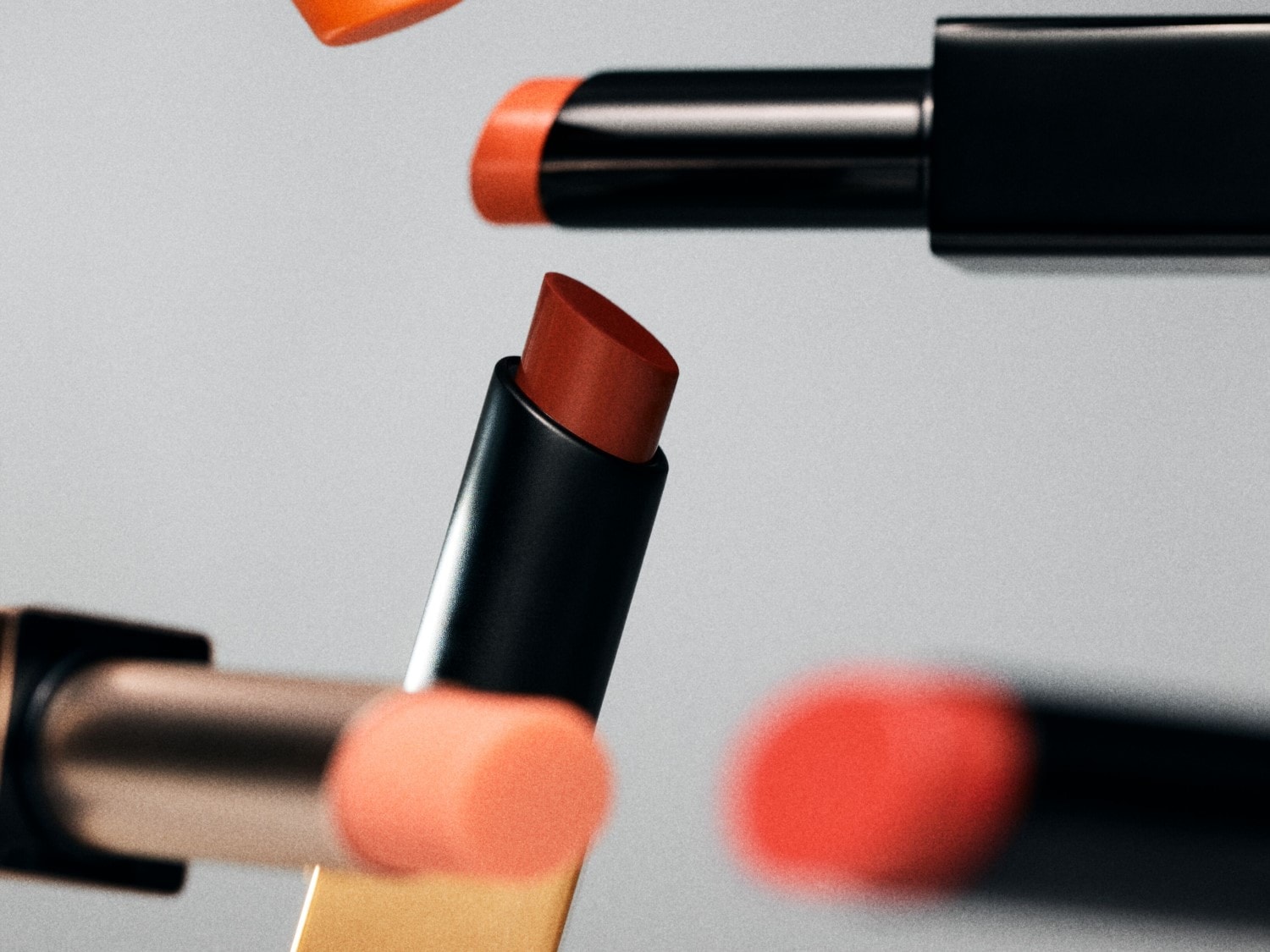 Nahaufnahme von Lippenstiften in verschiedenen Koralltönen mit glänzenden, schwarzen und goldenen Hülsen.