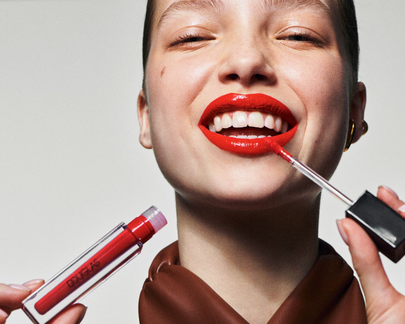 Eine strahlende Frau mit einem roten Douglas Lipgloss, der ihren Lippen einen glänzenden Look verleiht.