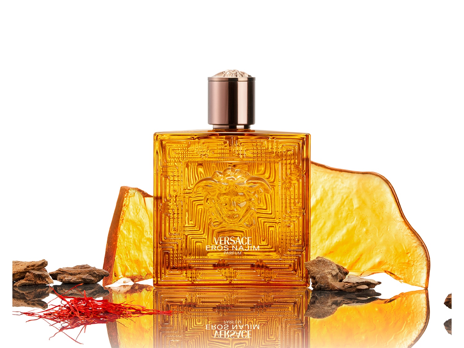 Gouden vierkante Versace Eros parfumfles met een reliëf van het Versace logo, omringd door amberkleurige stukken en rode saffraandraadjes.