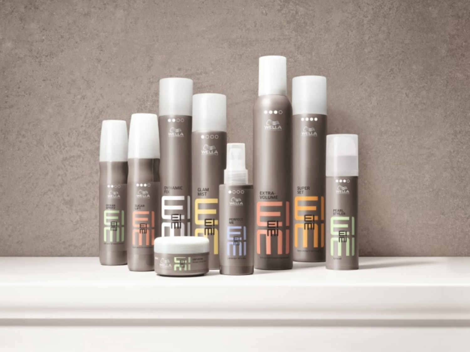 Eine Kollektion von Wella EIMI-Stylingprodukten, darunter Haarsprays, Mousse und Cremes, die auf einem Regal vor einem grauen Hintergrund präsentiert werden.