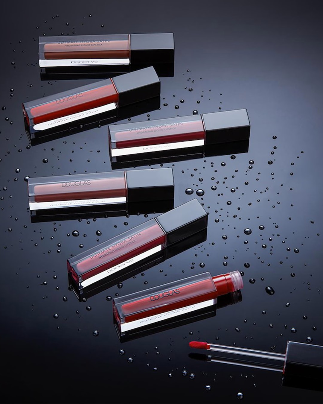 Entdecke Douglas Ultimate Hydra Satin feuchtigkeitsspendenden Flüssiglippenstift in verschiedenen Farbtönen auf glänzend schwarzem Grund mit Wassertropfen.